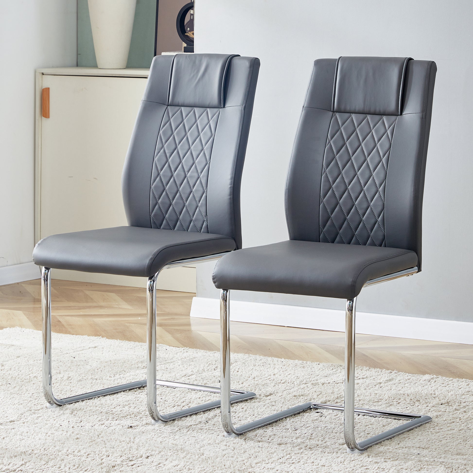 Two grey faux leather dining chairs with diamond stitching and chrome legs