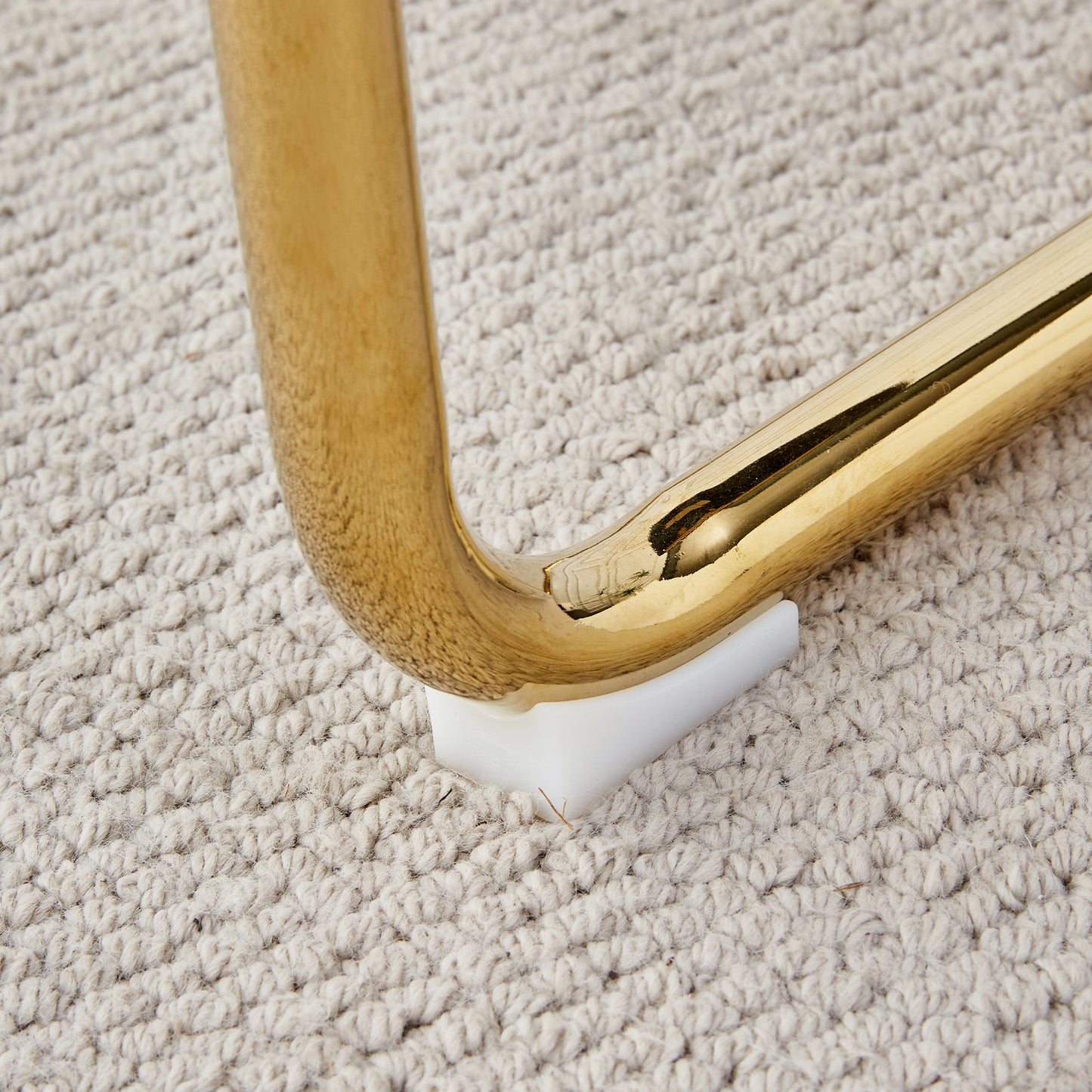 Shiny gold metal chair leg resting on a textured beige carpet