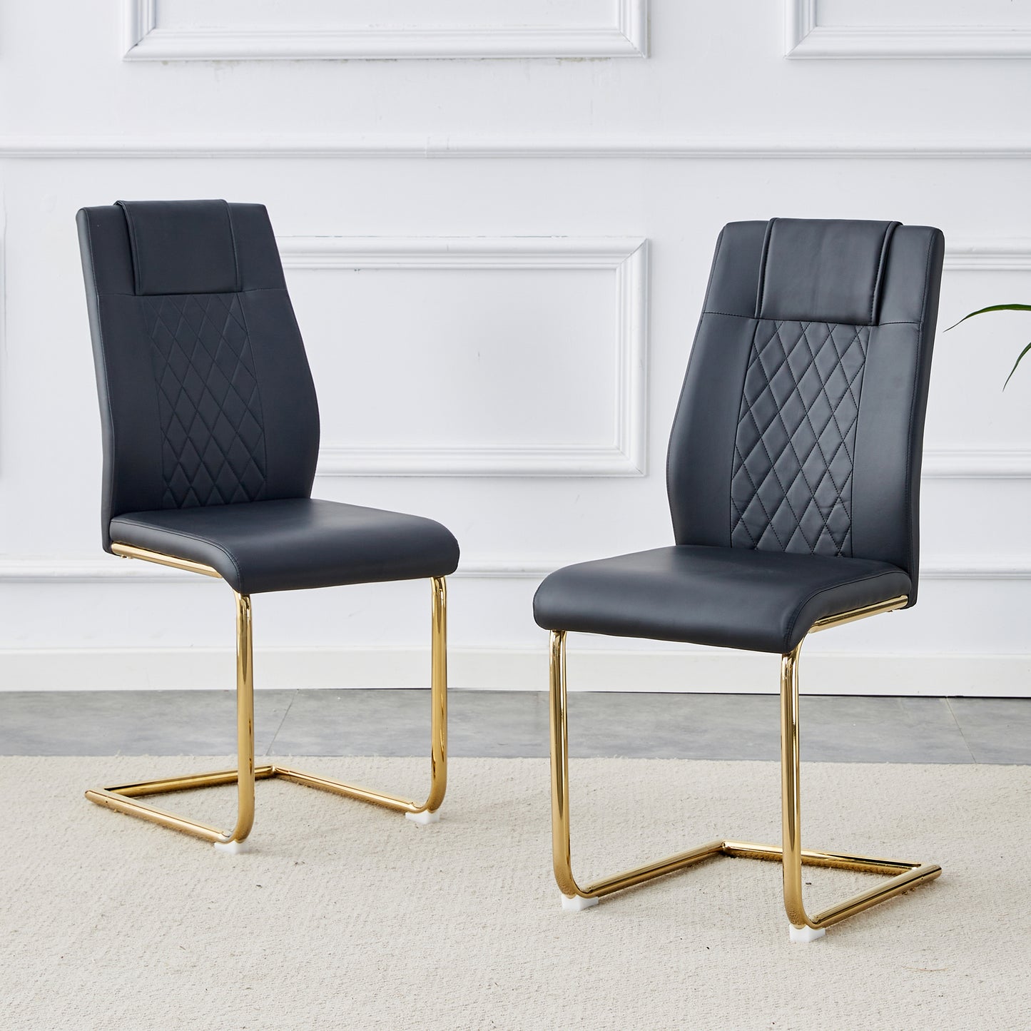 Two black faux leather dining chairs with gold cantilever bases and diamond tufting