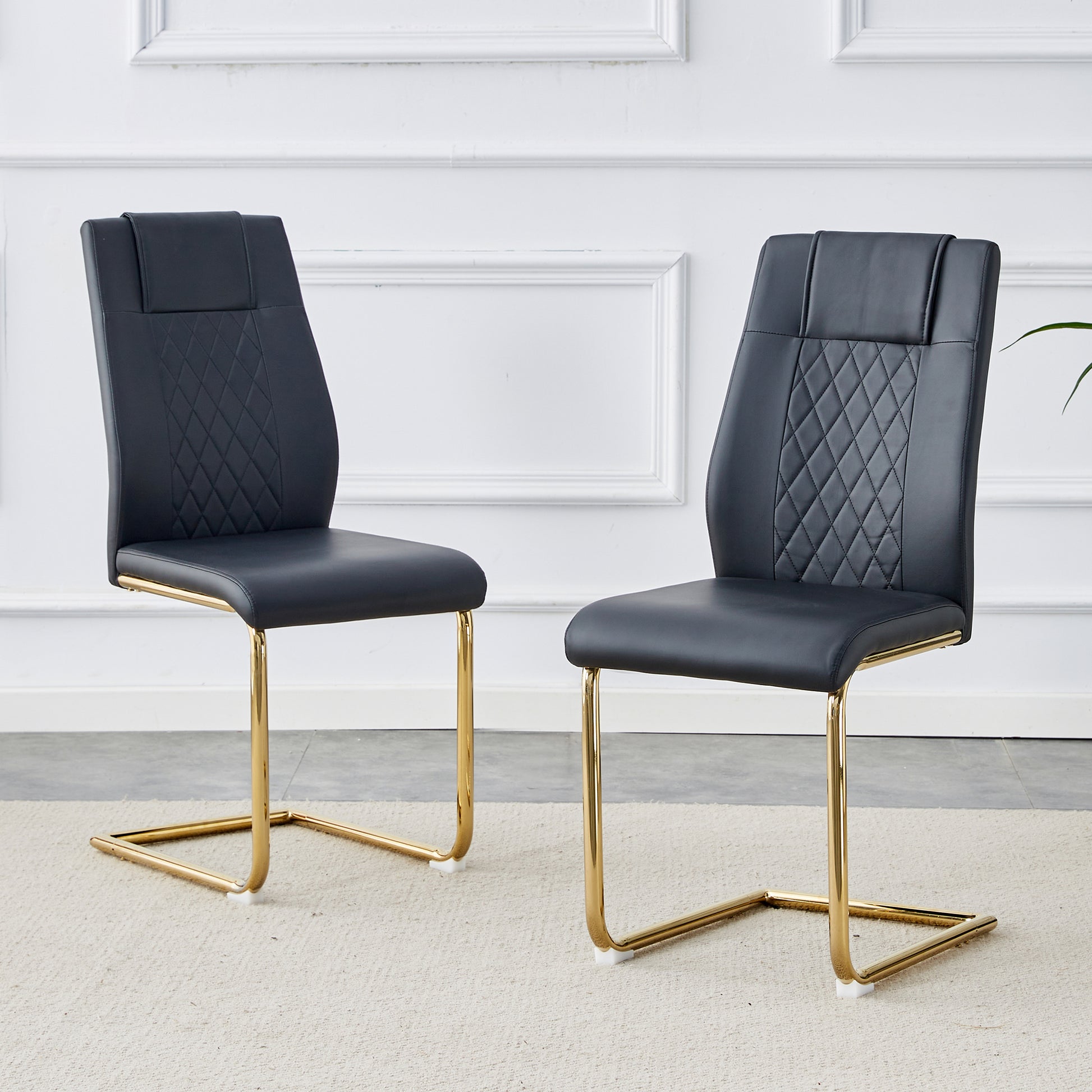 Two black faux leather dining chairs with gold cantilever bases and diamond tufting