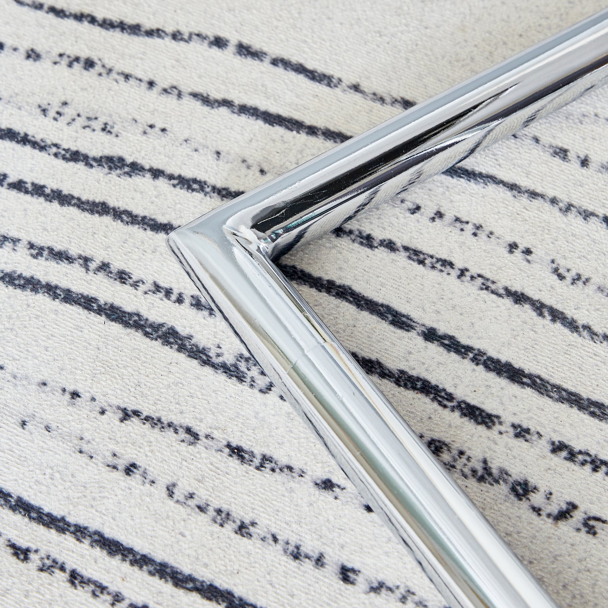 Polished chrome table leg corner detail on a striped rug