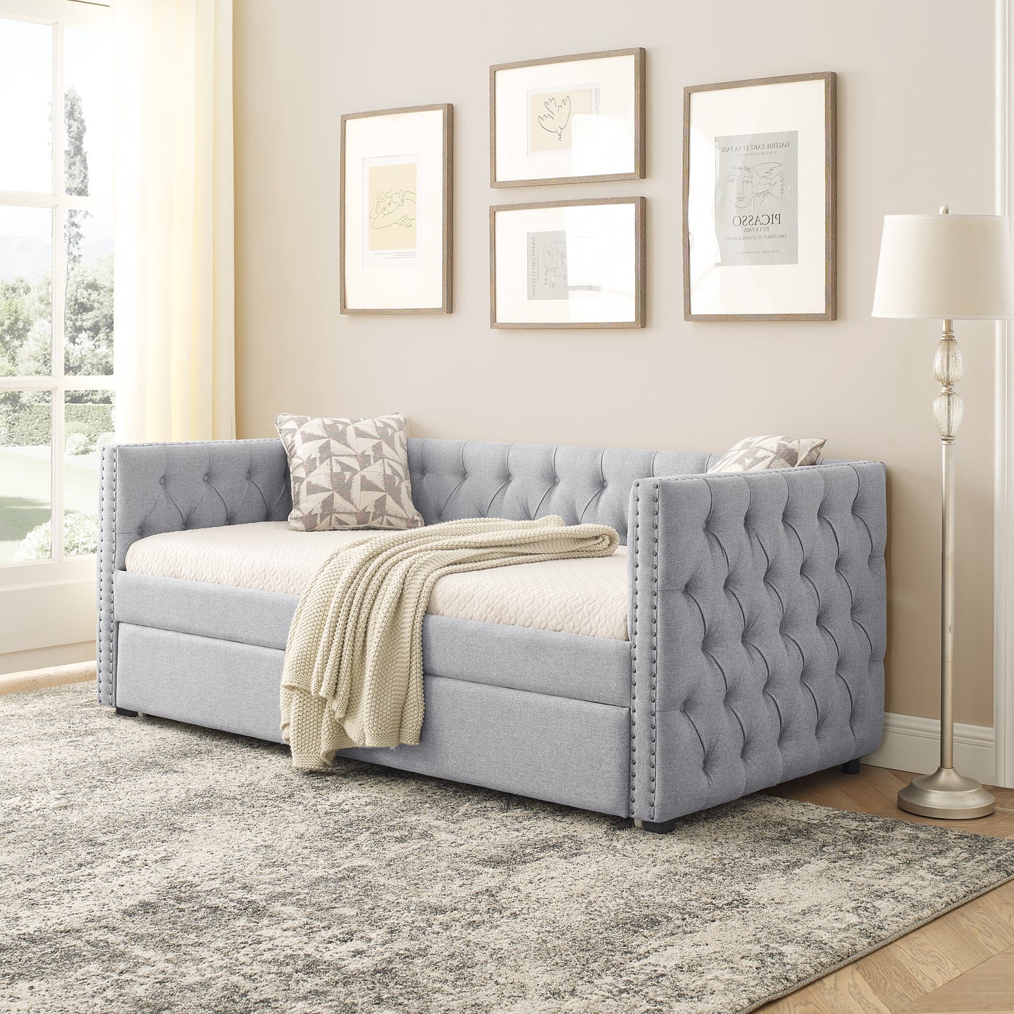 Tufted grey fabric daybed with silver nailhead trim and cream throw