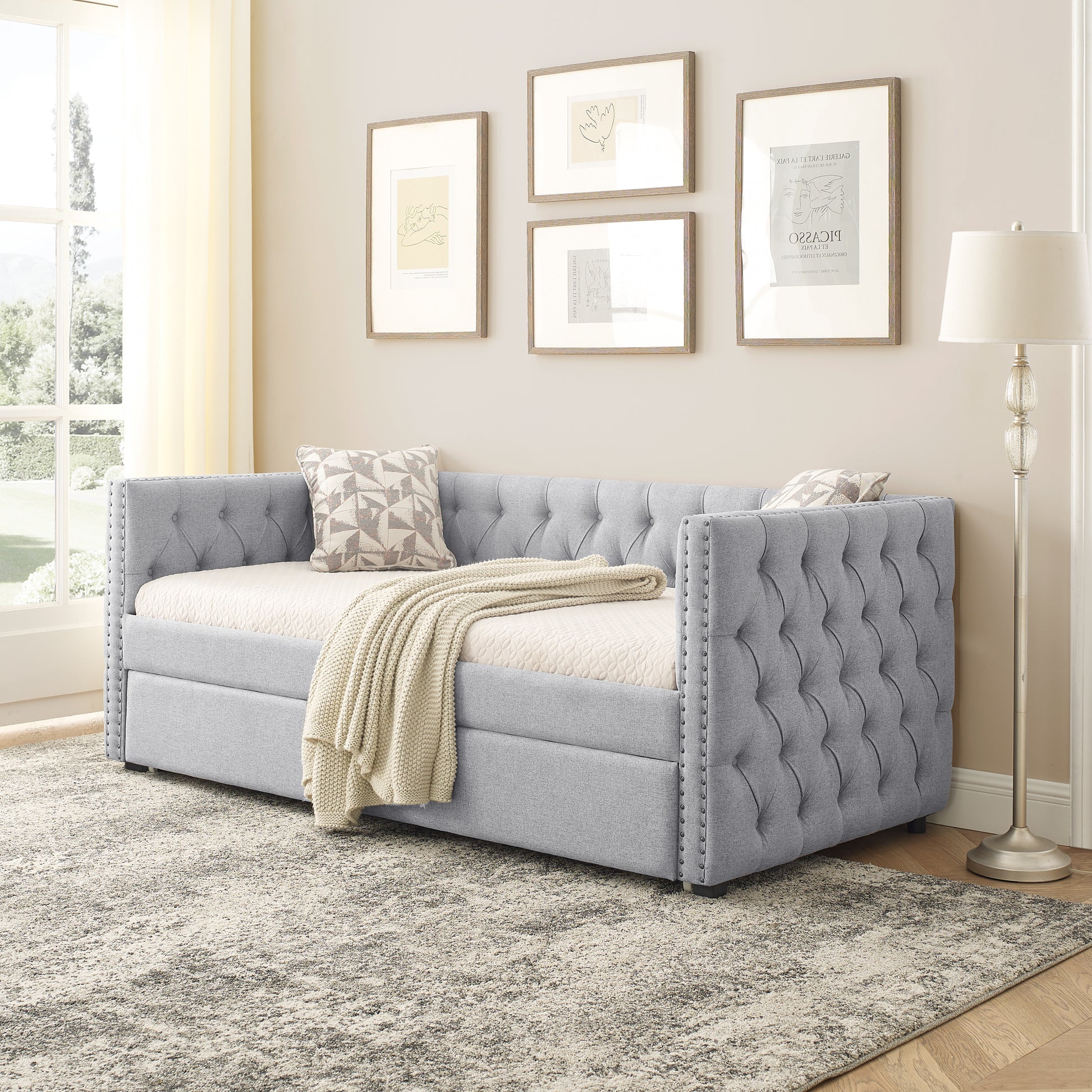 Tufted grey fabric daybed with silver nailhead trim and cream throw