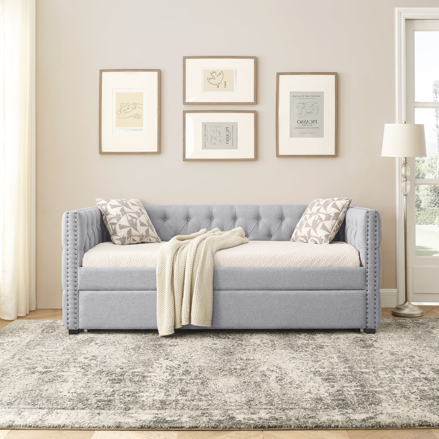 Light gray tufted daybed with nailhead trim and cream knitted throw