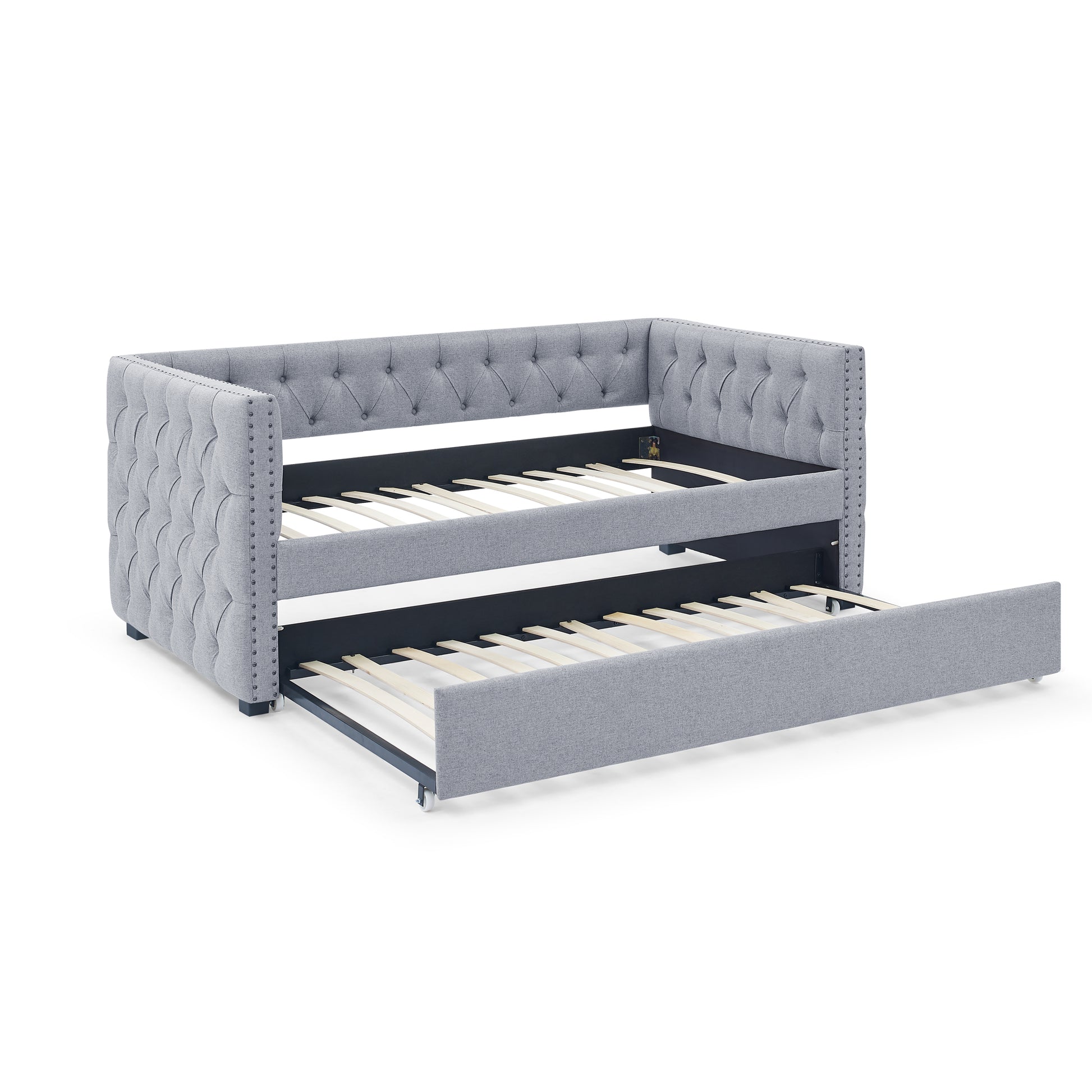 Tufted grey fabric daybed with trundle pulled out featuring nailhead trim and wooden slats
