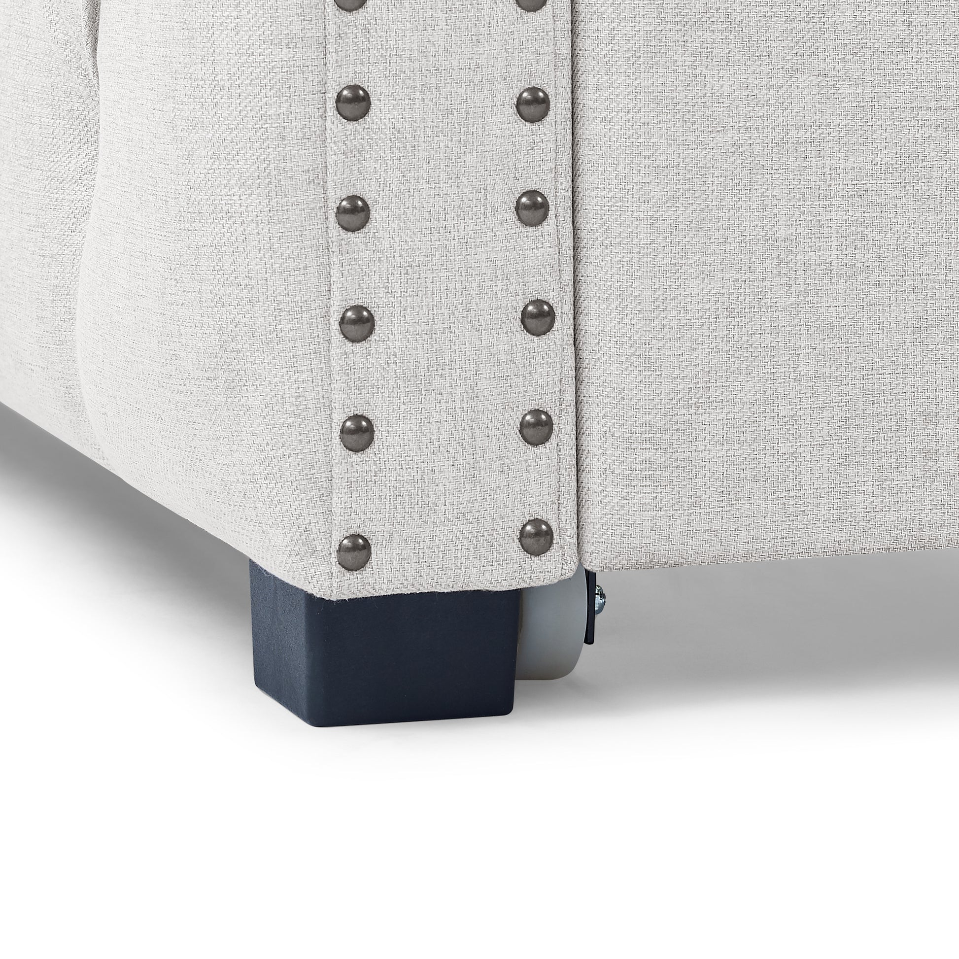 Closeup of light grey textured fabric sofa with studded trim and dark blue legs