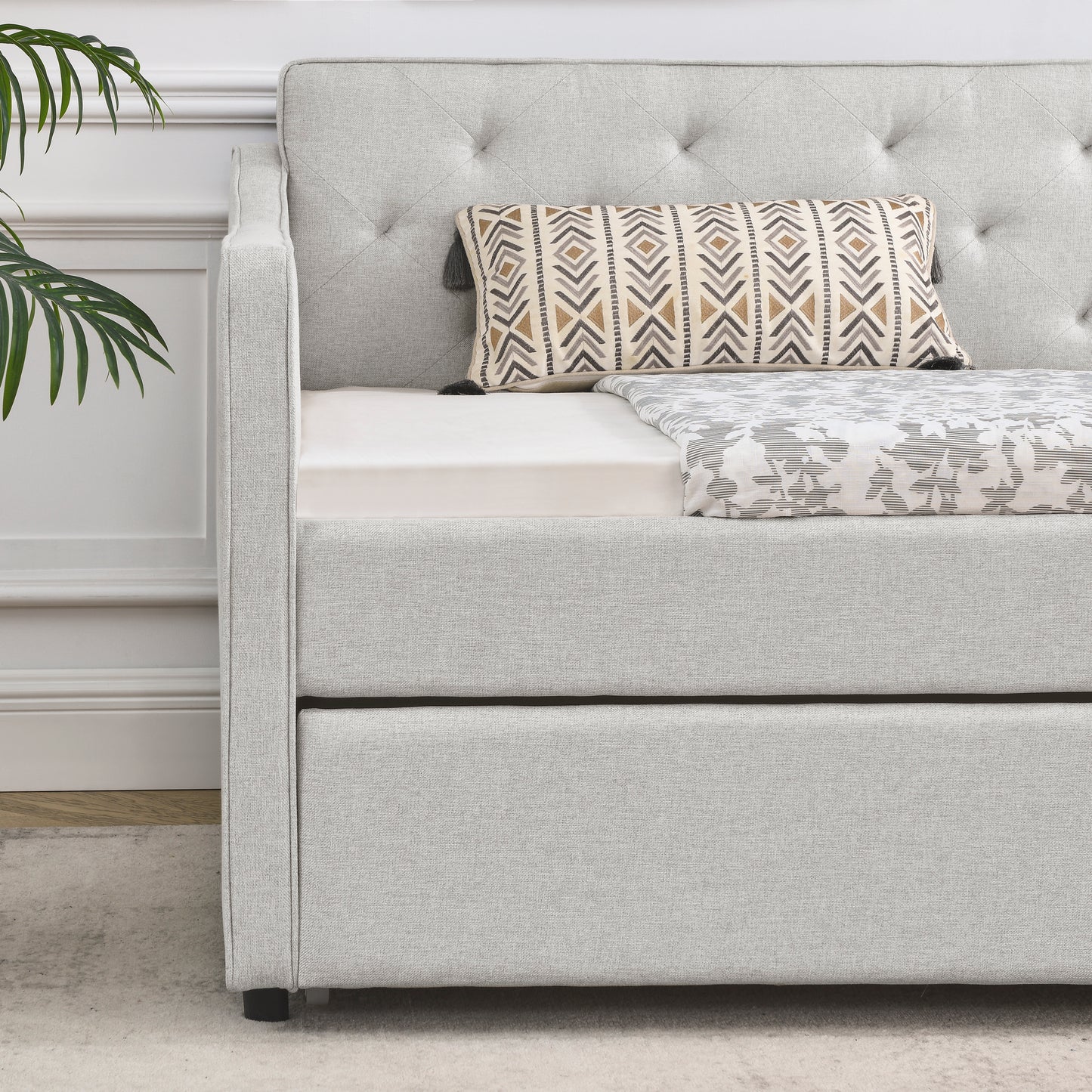 Light gray linen upholstered daybed with tufted back and pullout trundle