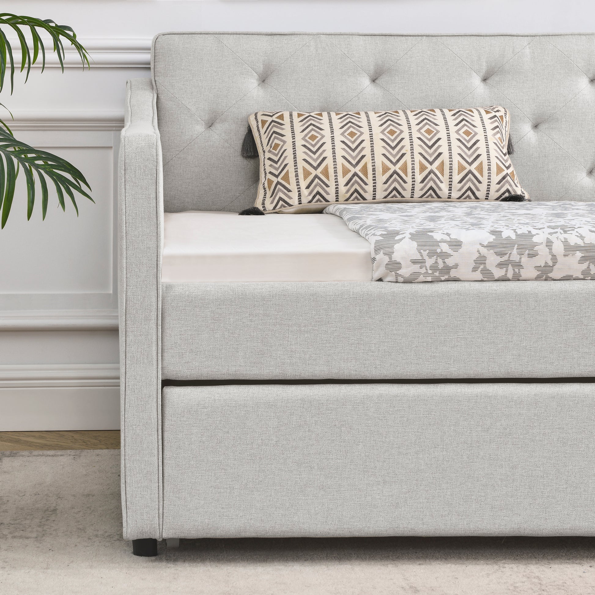 Light gray linen upholstered daybed with tufted back and pullout trundle