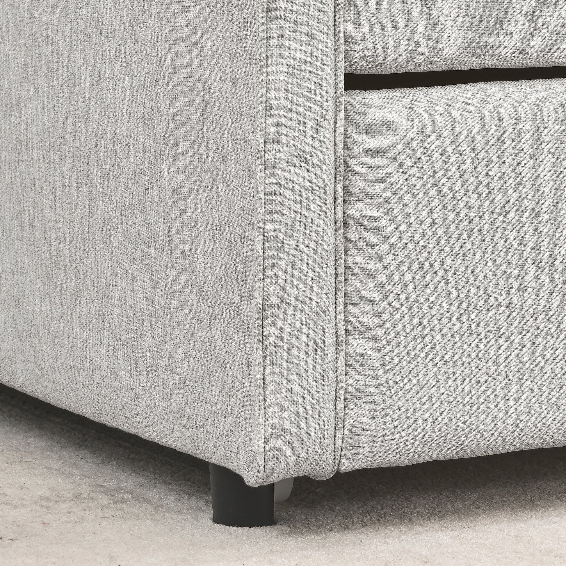 Closeup of light grey woven fabric upholstery on a sofa corner with black leg