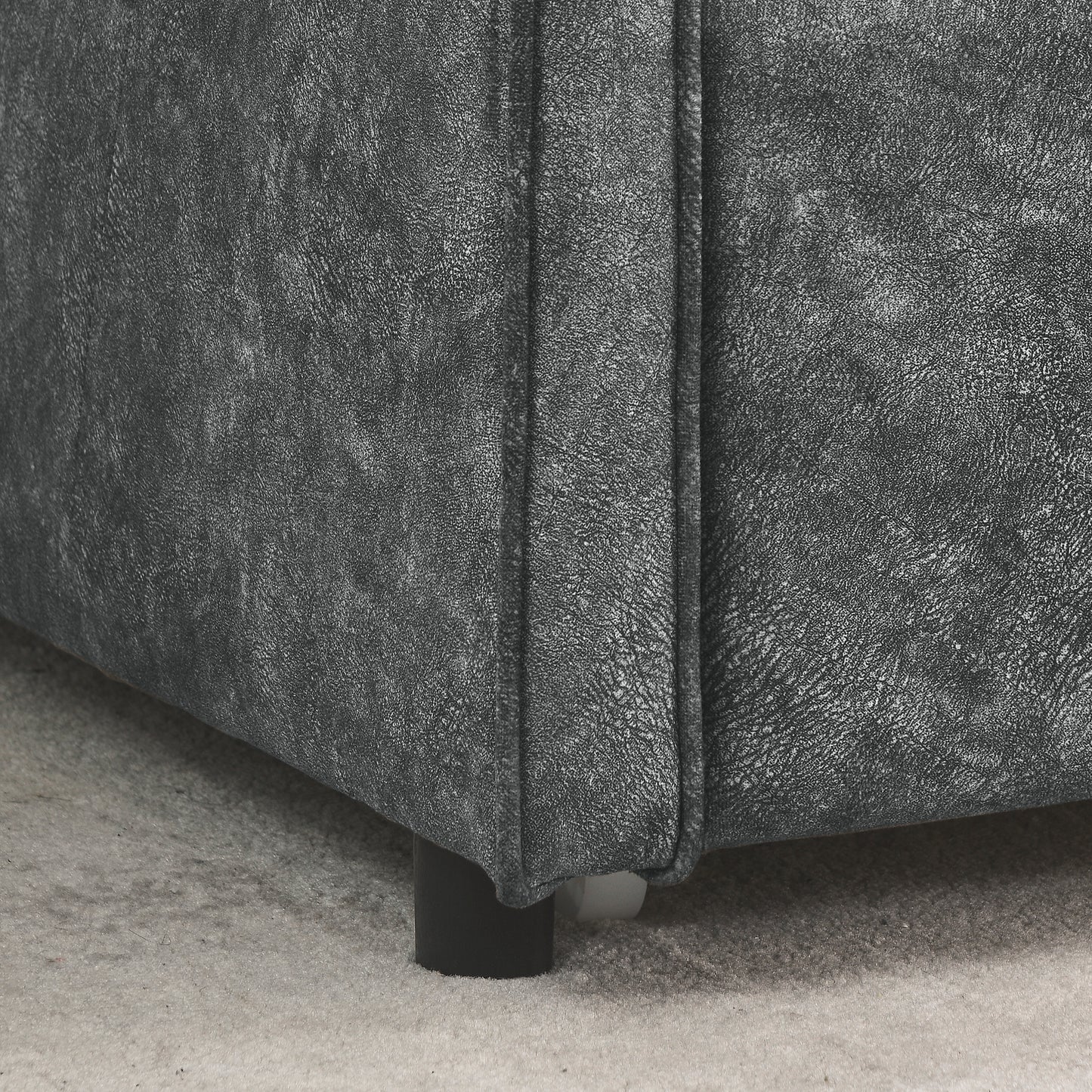 Closeup of textured charcoal gray faux leather upholstery on a sofa armrest