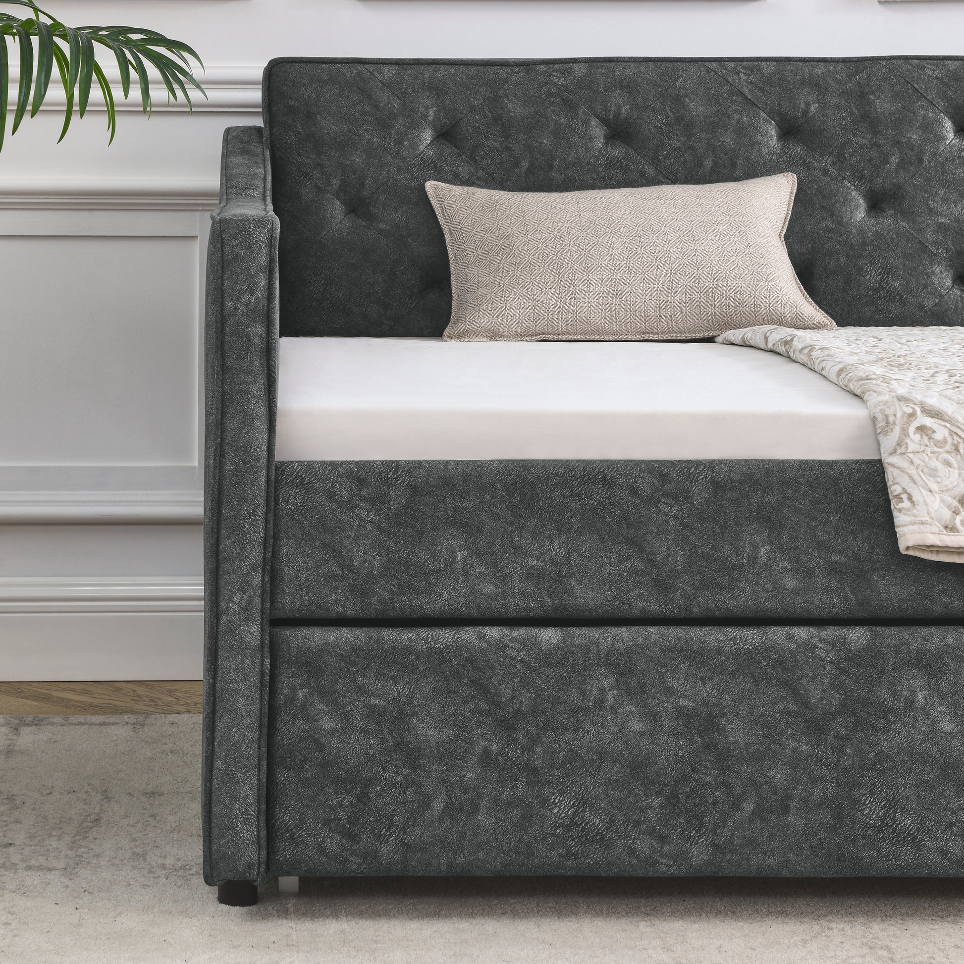 Dark gray faux leather tufted daybed with a cream patterned pillow