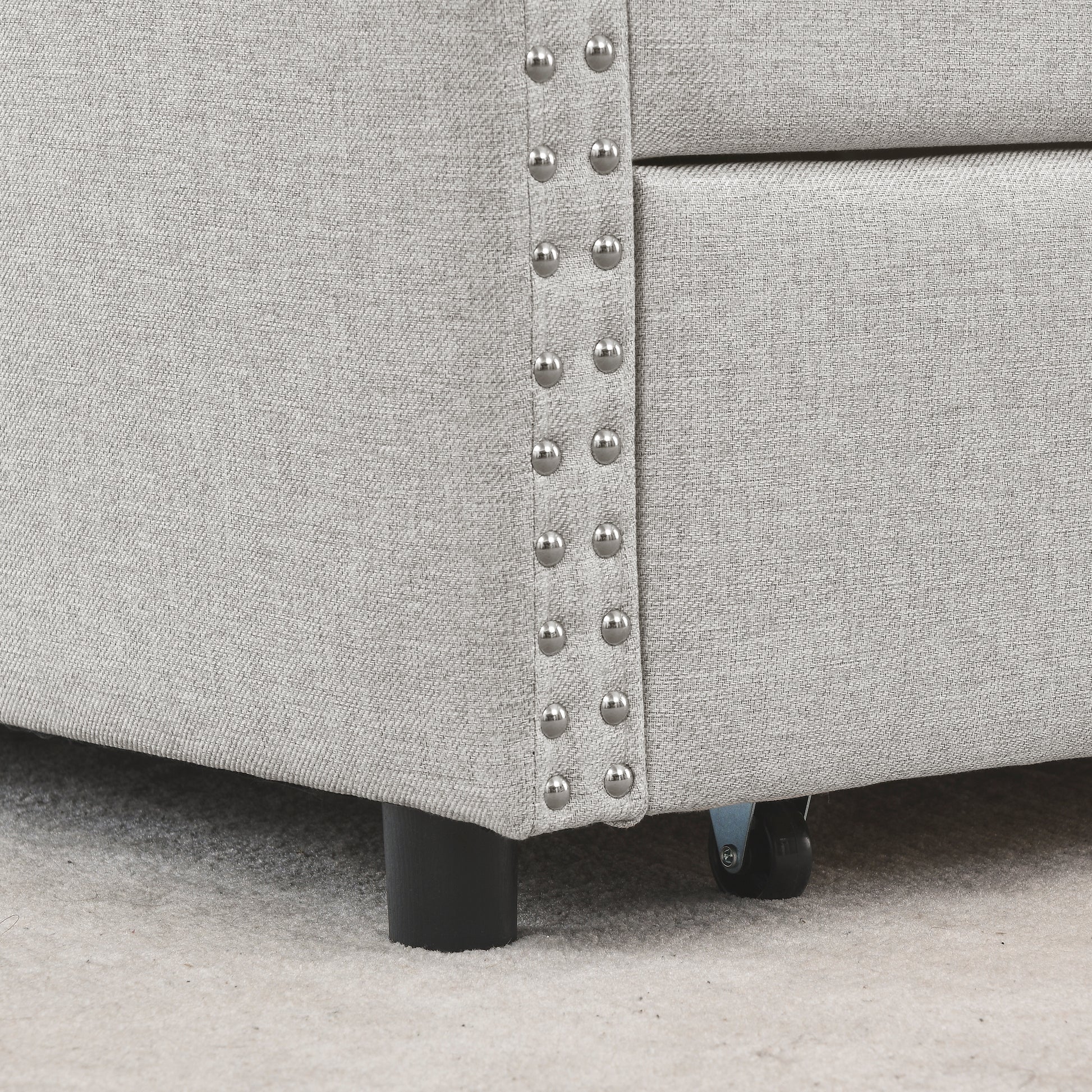 Closeup of light grey linen fabric with decorative silver nailhead trim on a sofa base