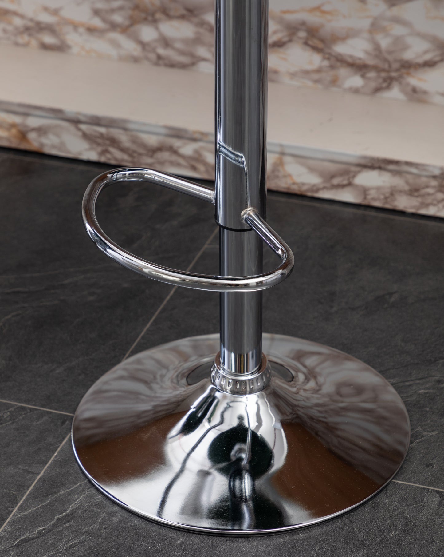 Polished chrome bar stool base with circular footrest on dark tiled floor