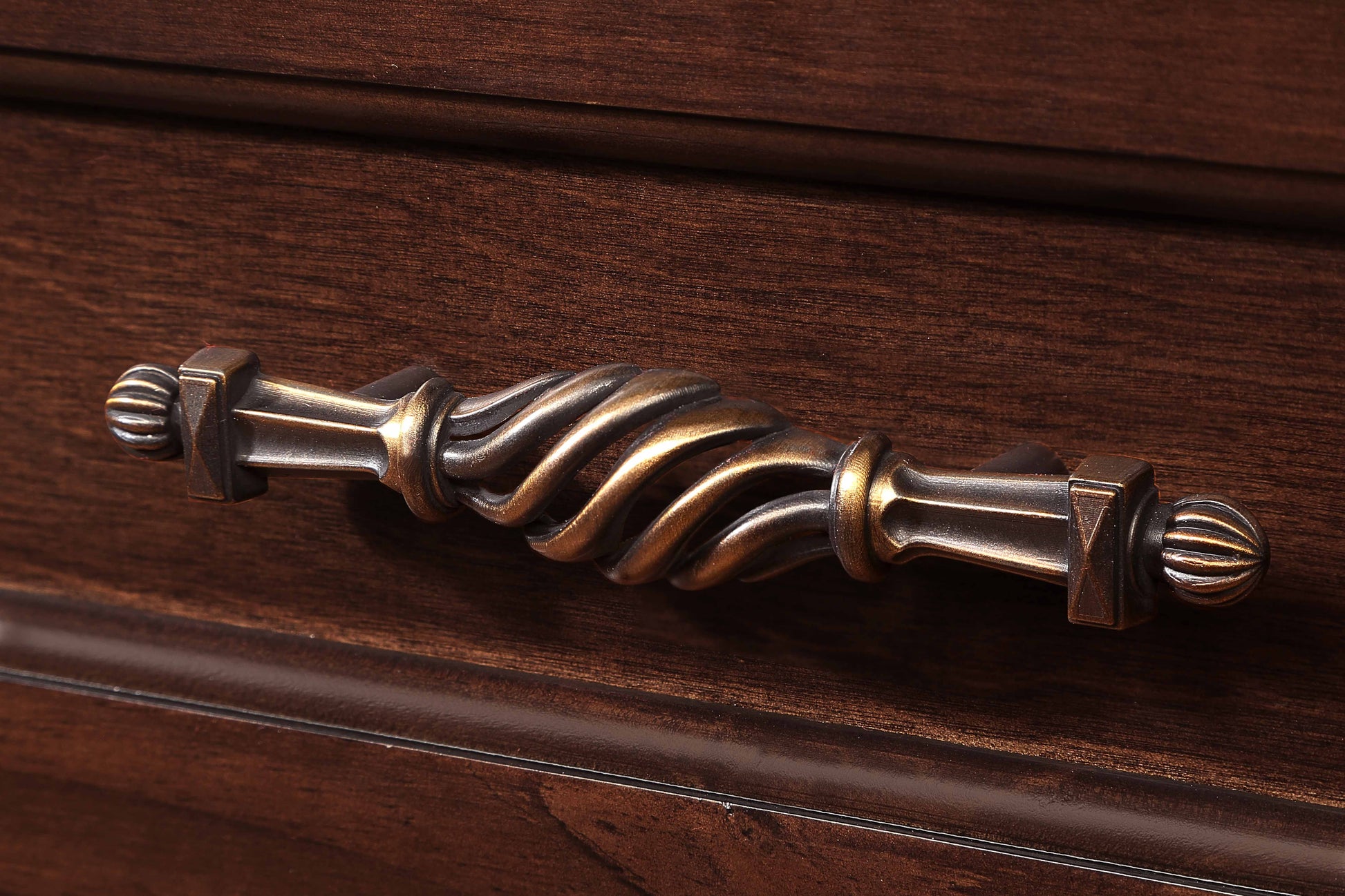 Antique brass drawer pull with ornate twisted design on dark wood
