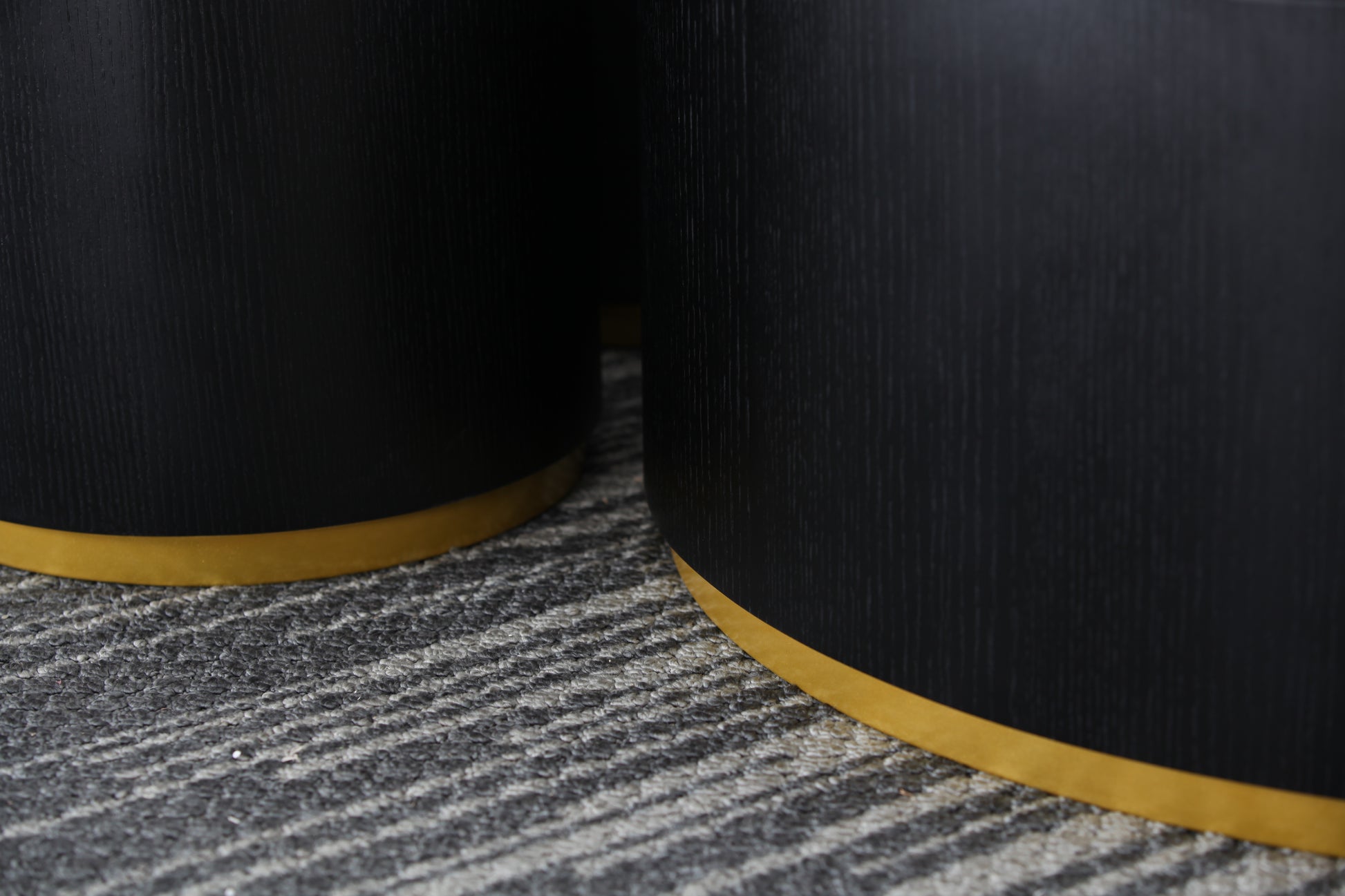 Closeup of a black cylindrical side table with a brushed gold base on a textured rug