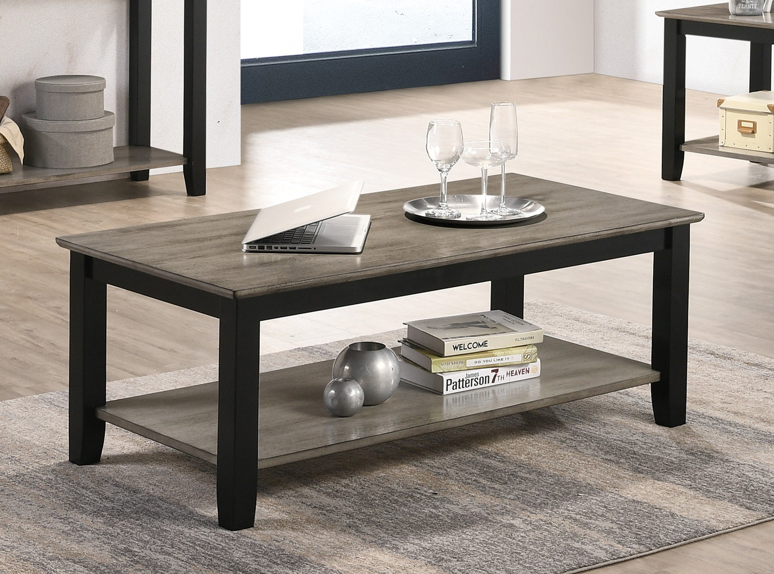 Modern gray wood coffee table with black frame and two tiers featuring a laptop and wine glasses