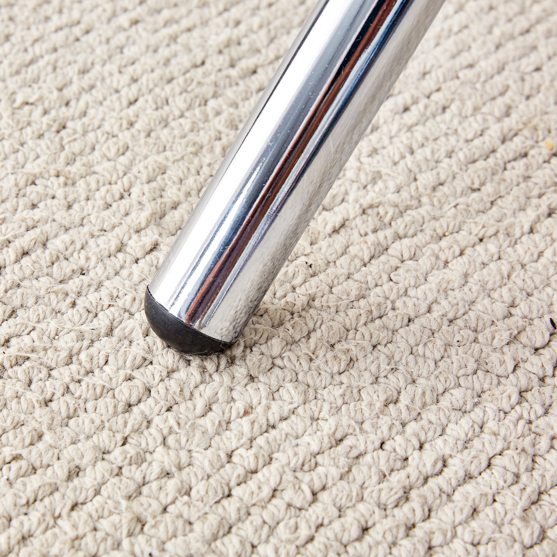 Chrome chair leg with black rubber foot on textured beige rug