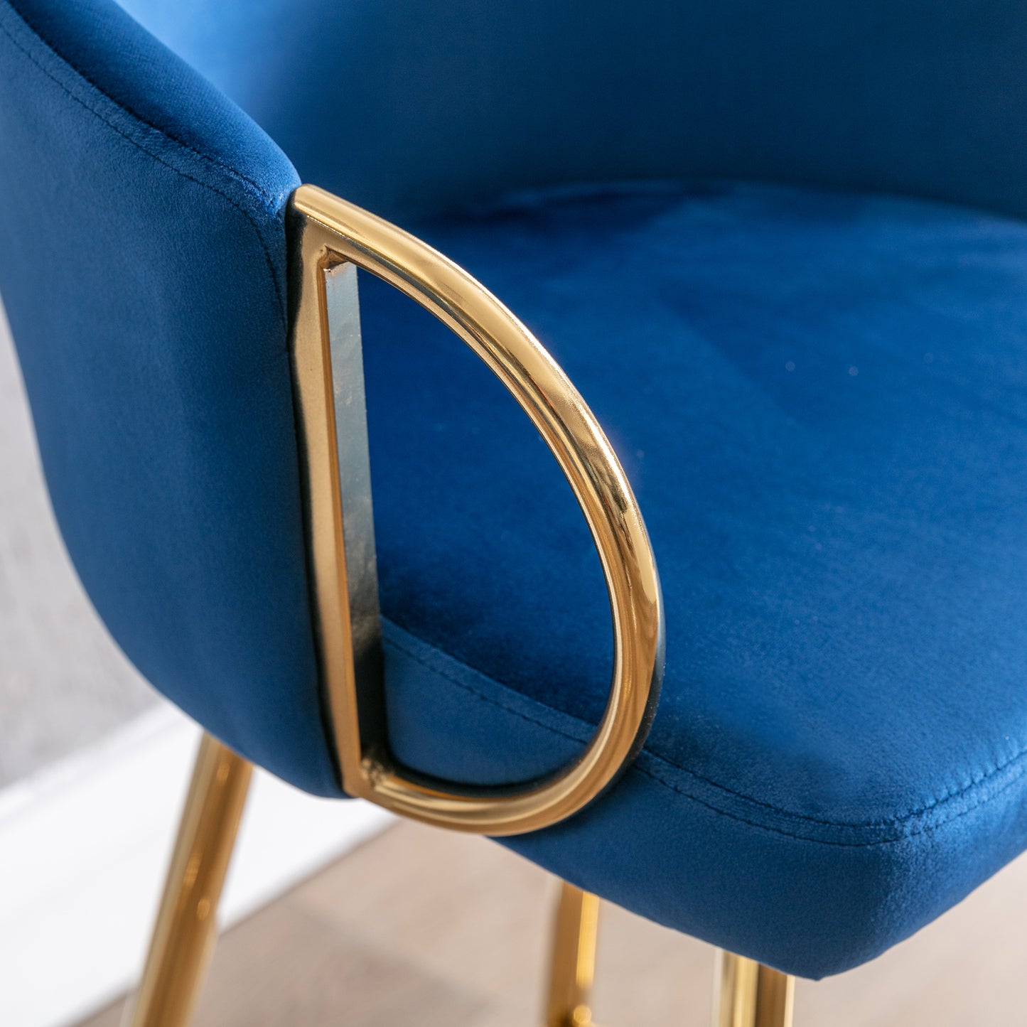 Closeup of plush navy blue velvet armchair armrest with polished gold metal accent