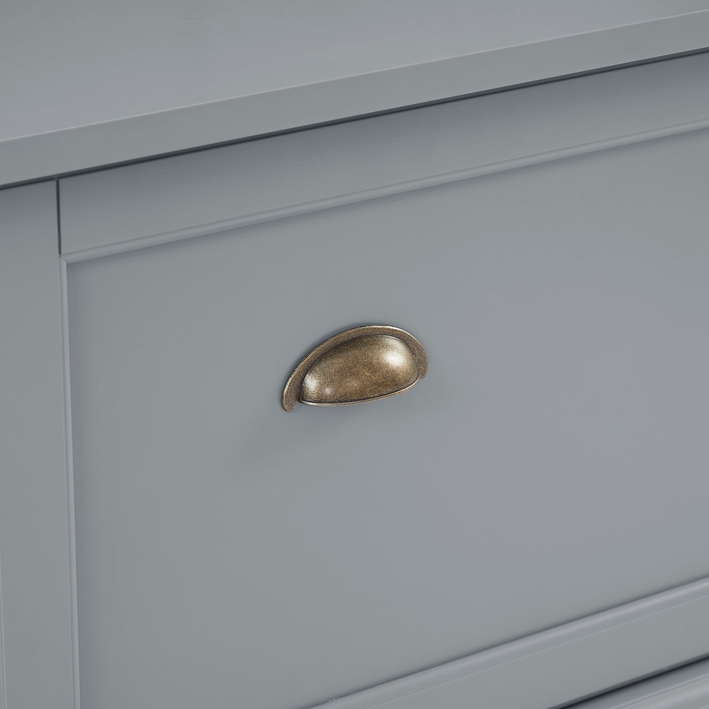 Antique brass cup pull on a gray dresser drawer