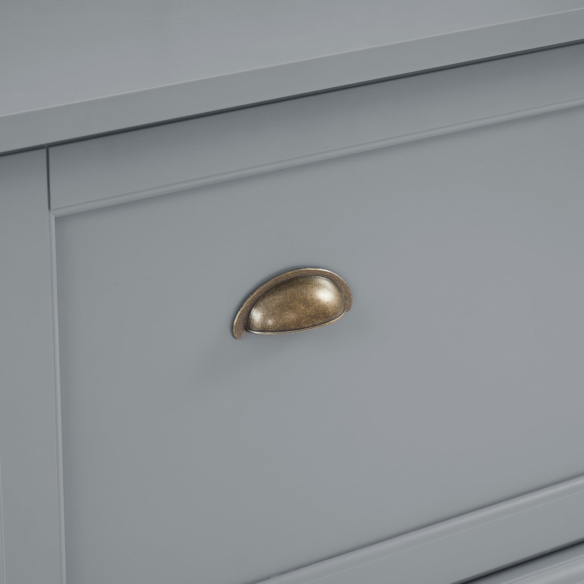 Antique brass cup pull on a gray dresser drawer
