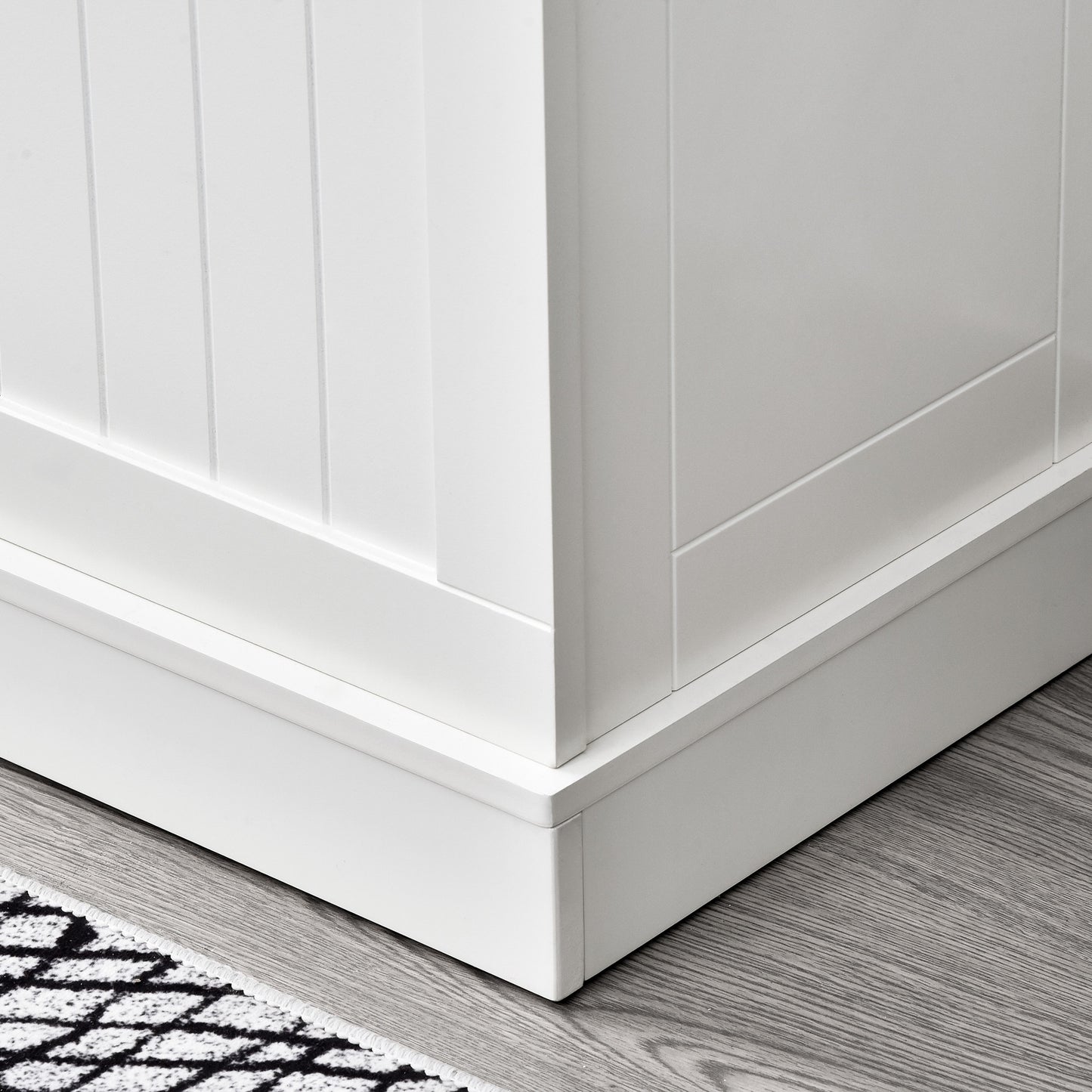 White paneled cabinet base with detailed trim on hardwood floor