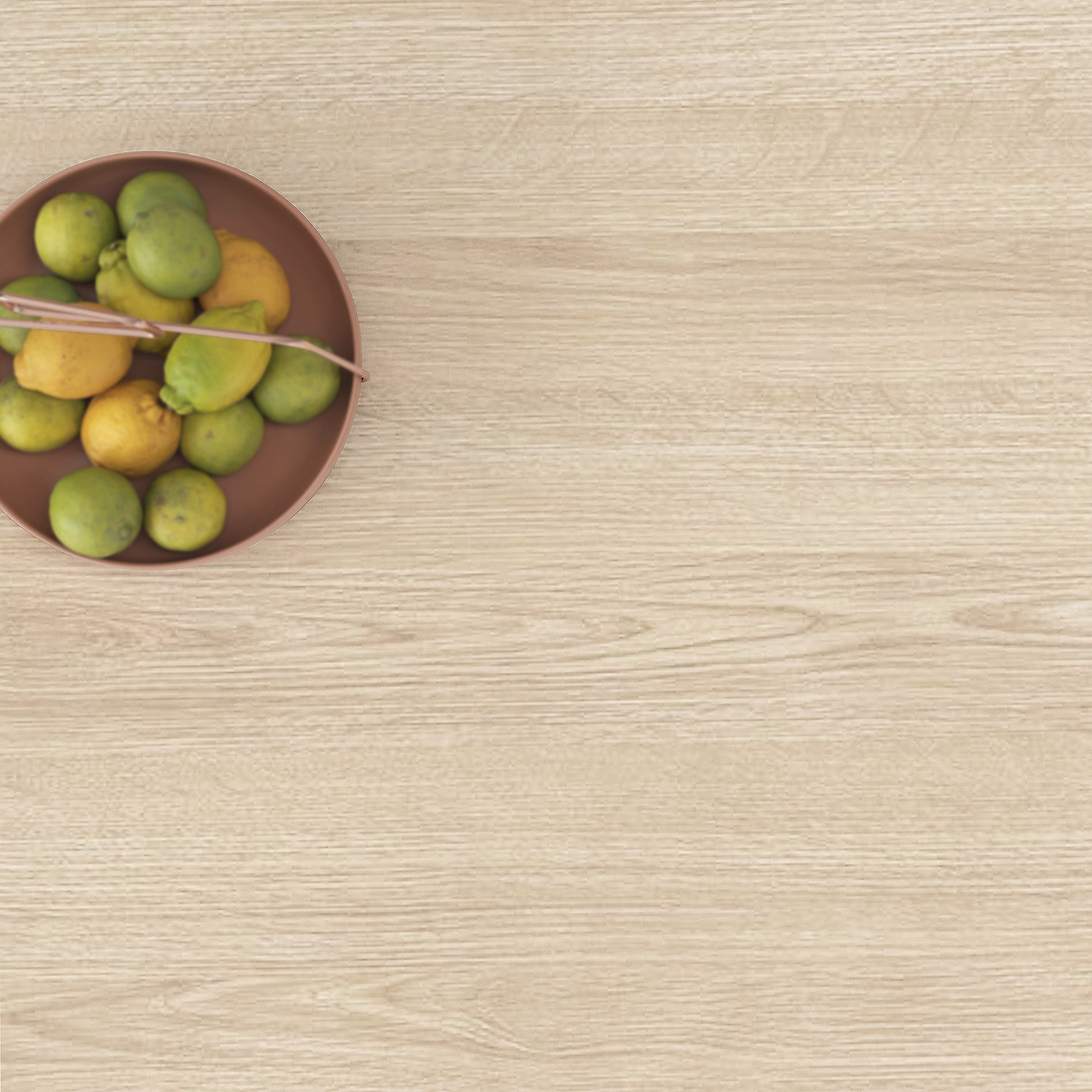 Round copper bowl filled with yellow and green lemons on a light wood grain background