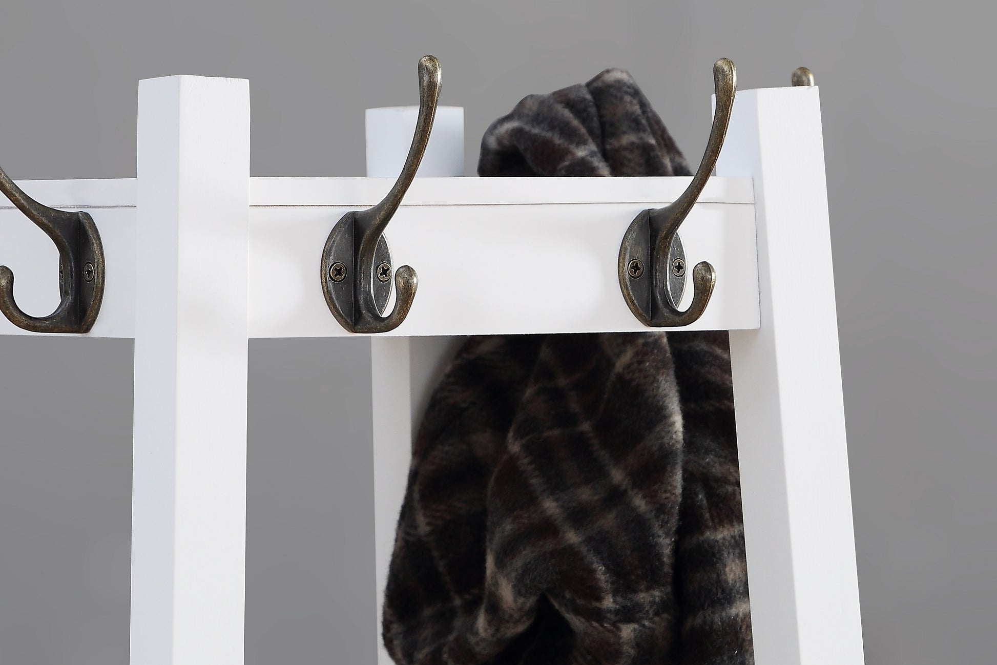 White wooden coat rack with antique brass hooks holding a patterned scarf