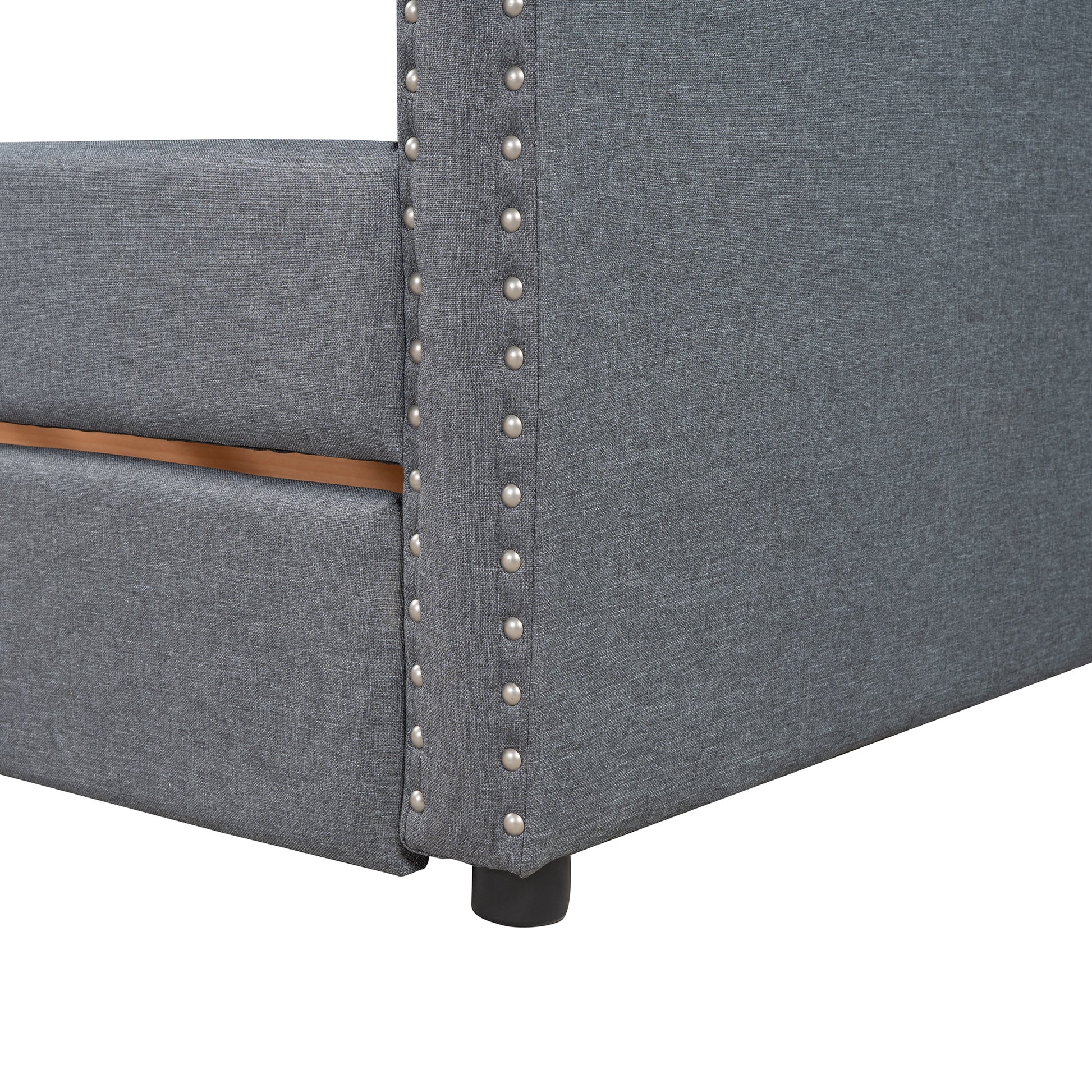 Gray upholstered bed frame corner with silver nailhead trim and wood accent