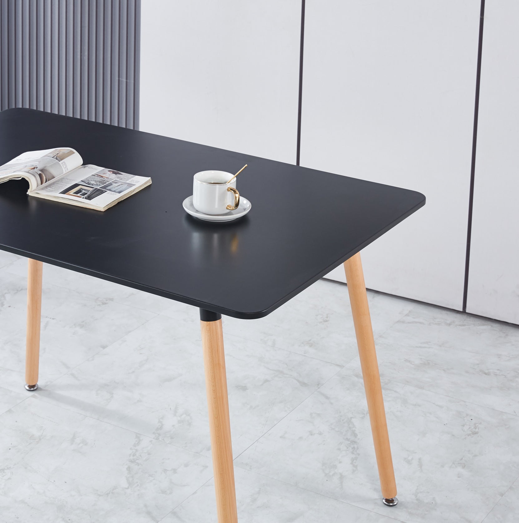 Black rectangular dining table with light wood legs and a coffee cup