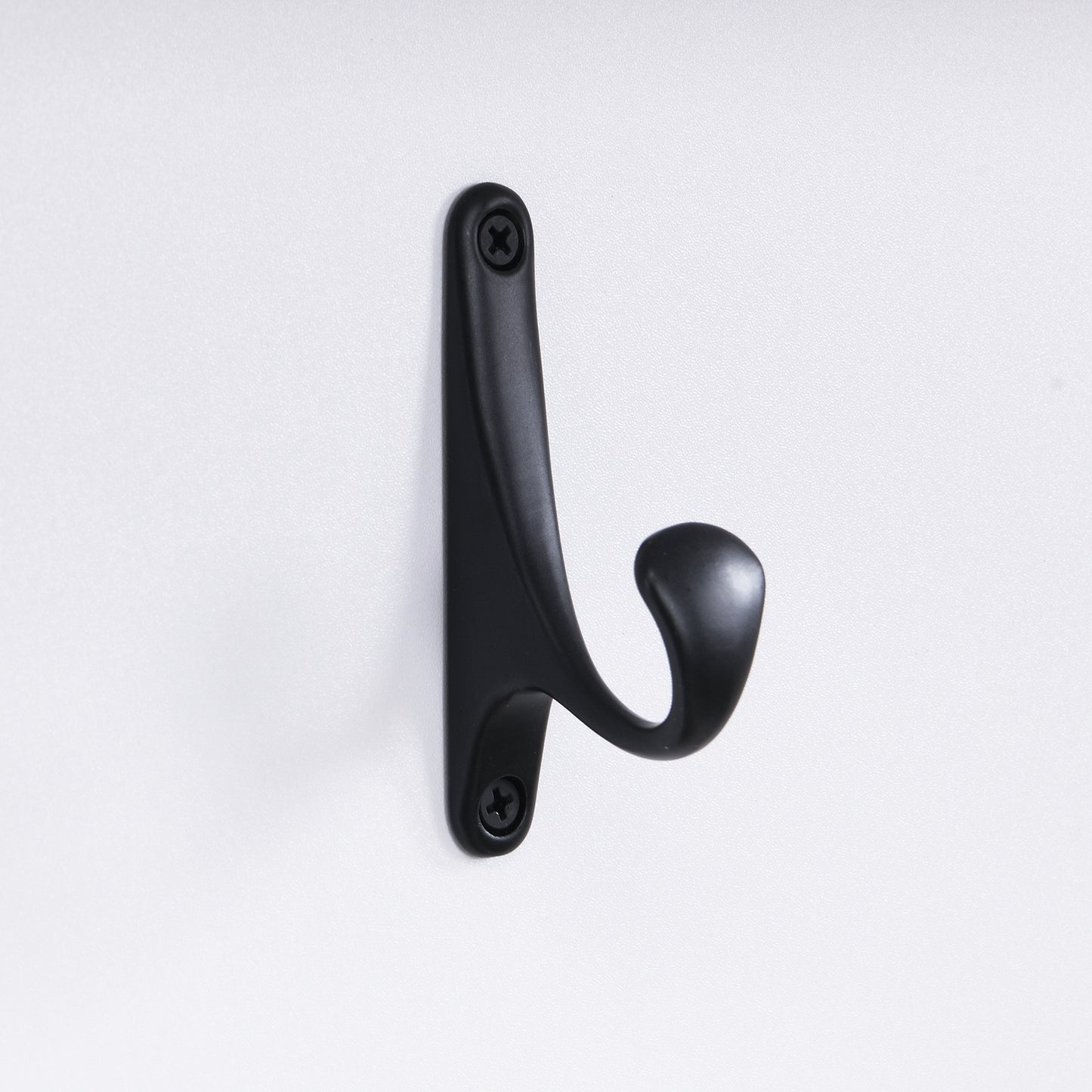 Black metal coat hook with curved design attached to a white surface with screws