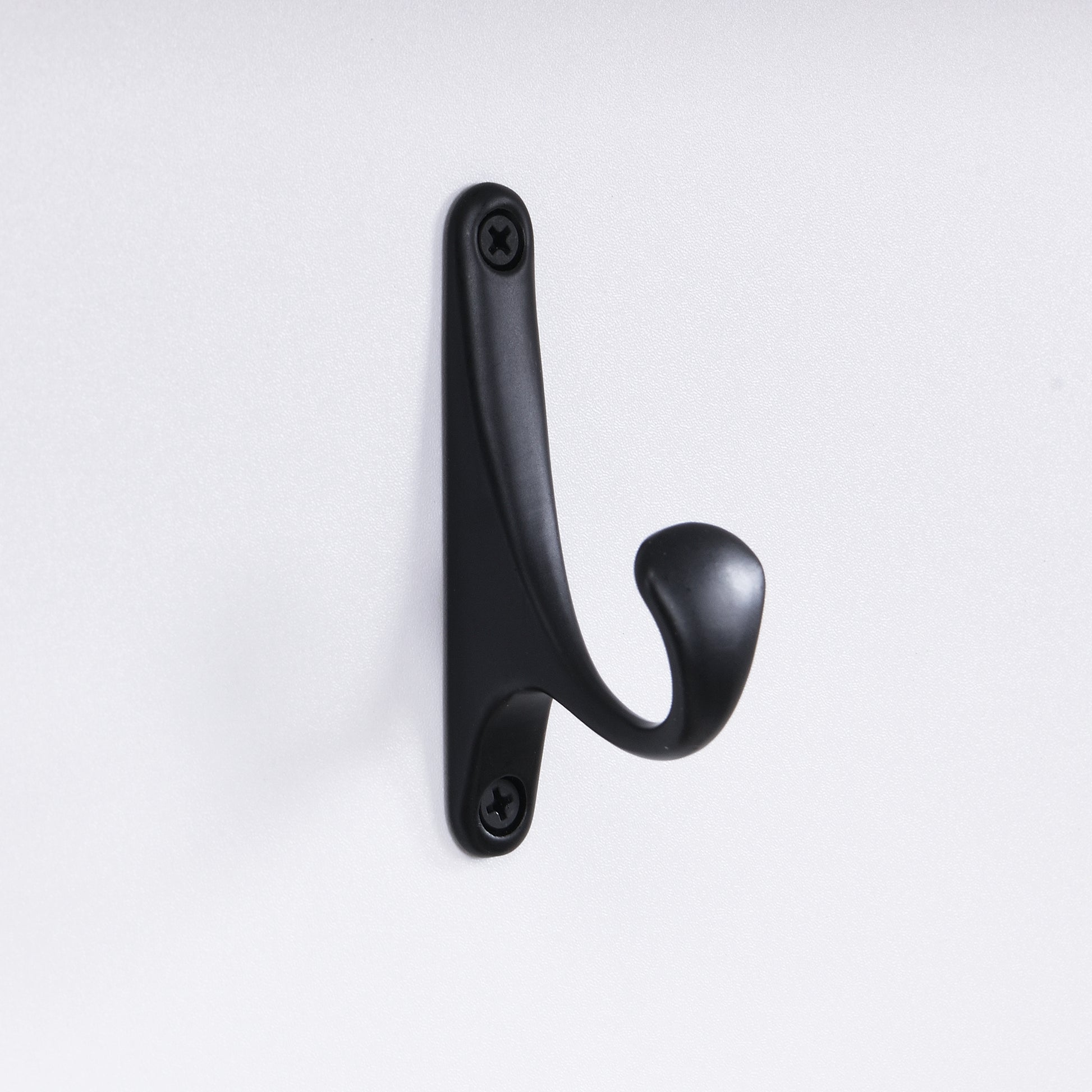 Black metal coat hook with curved design attached to a white surface with screws