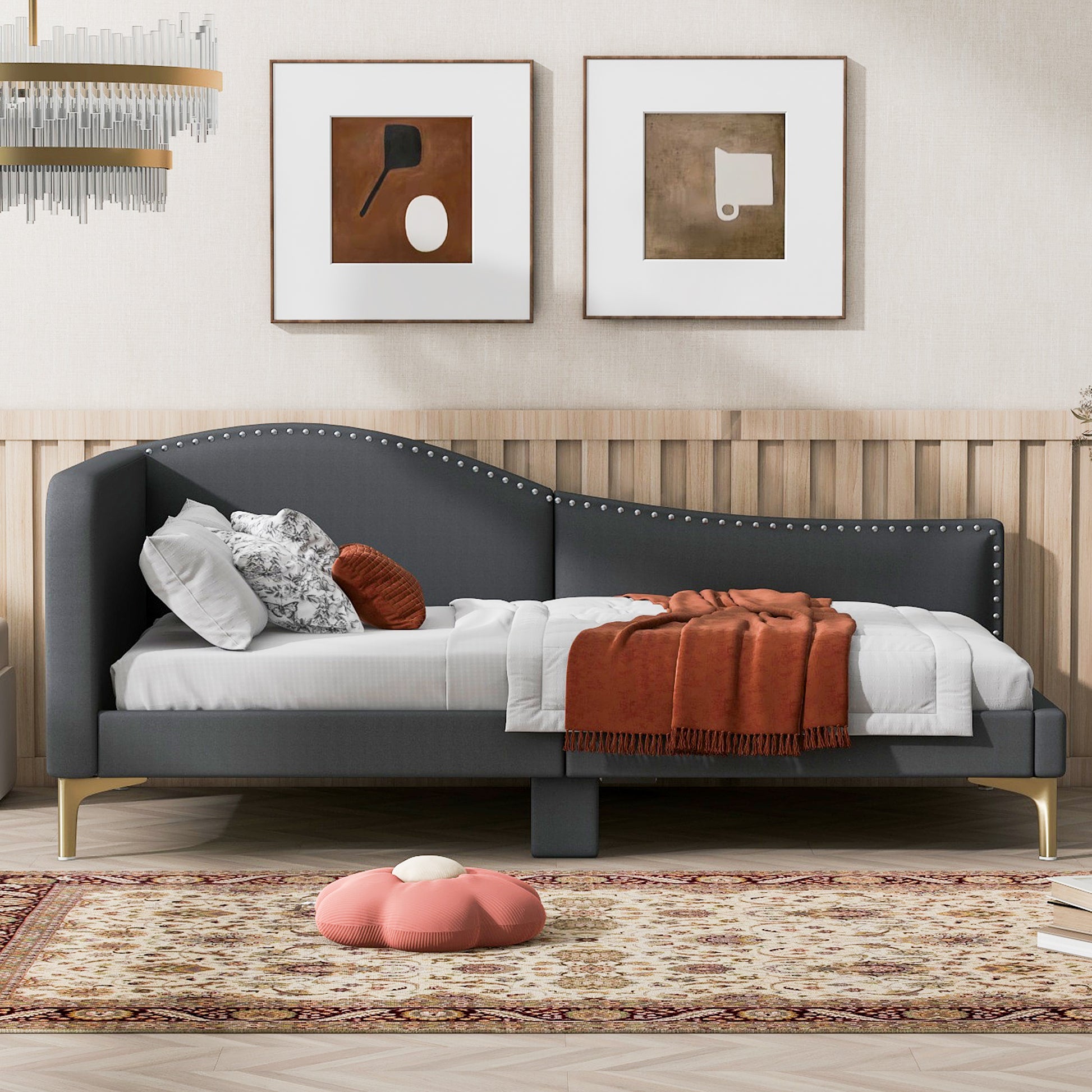 Dark gray tufted daybed with nailhead trim and gold legs styled with pillows and an orange throw blanket