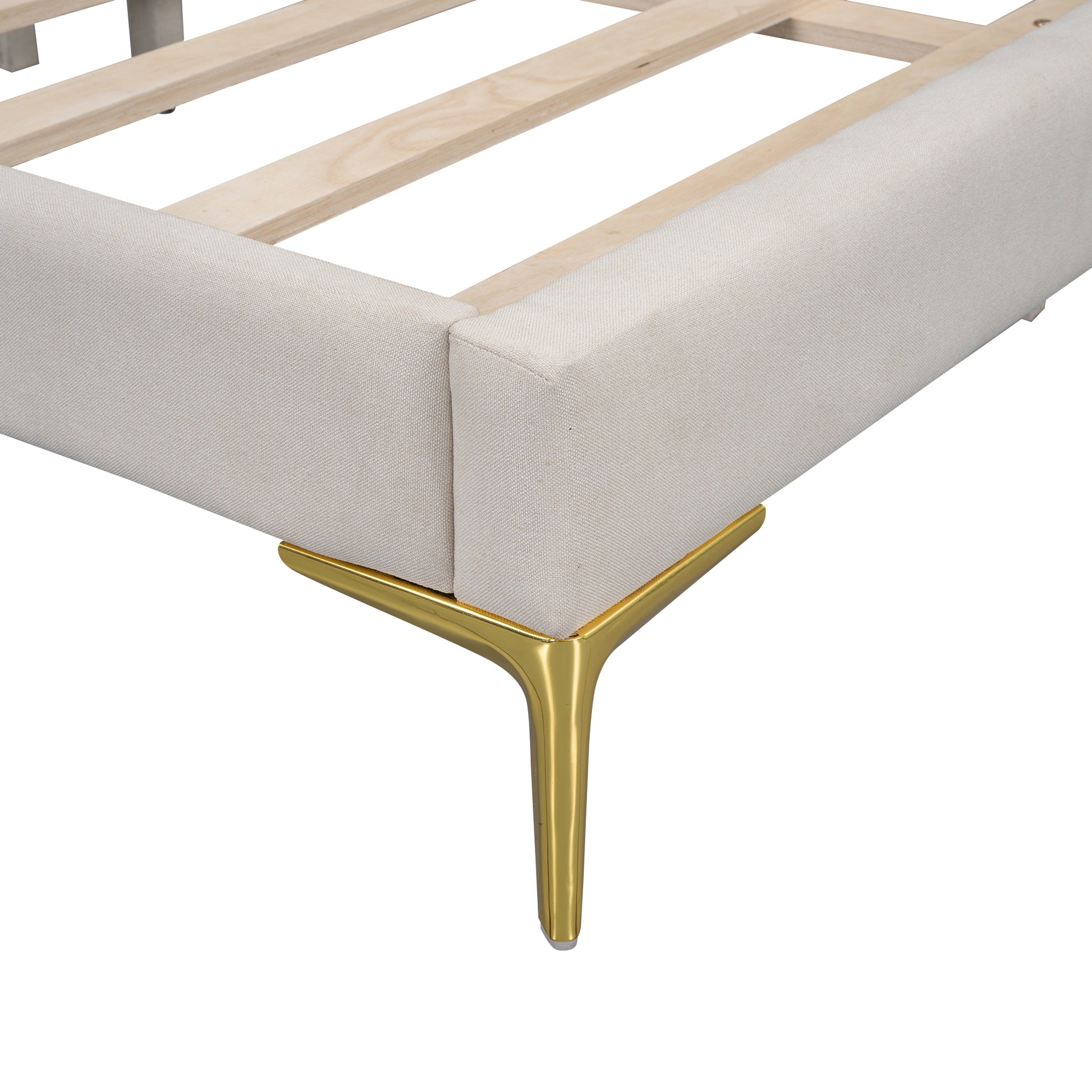 Closeup of a beige upholstered bed frame with a wooden slat support system and a gold tapered leg