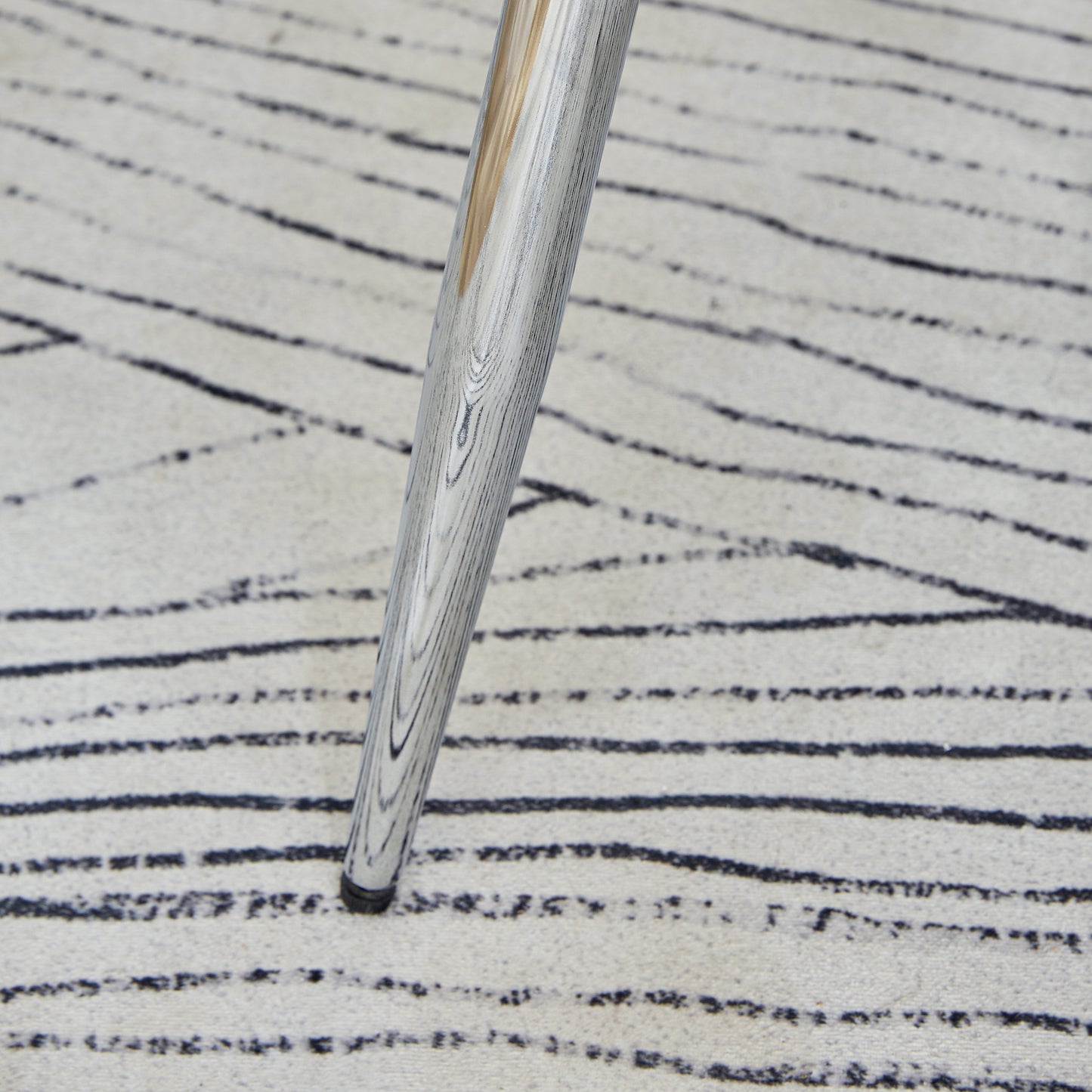Sleek silver chair leg with wood grain texture on a striped rug