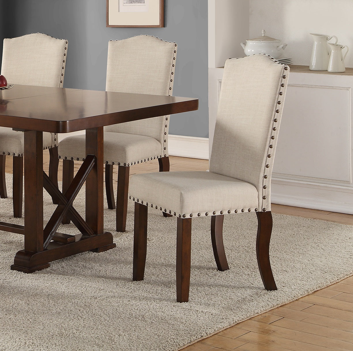 Upholstered dining chair in beige linen fabric with brass nailhead trim and dark wood legs