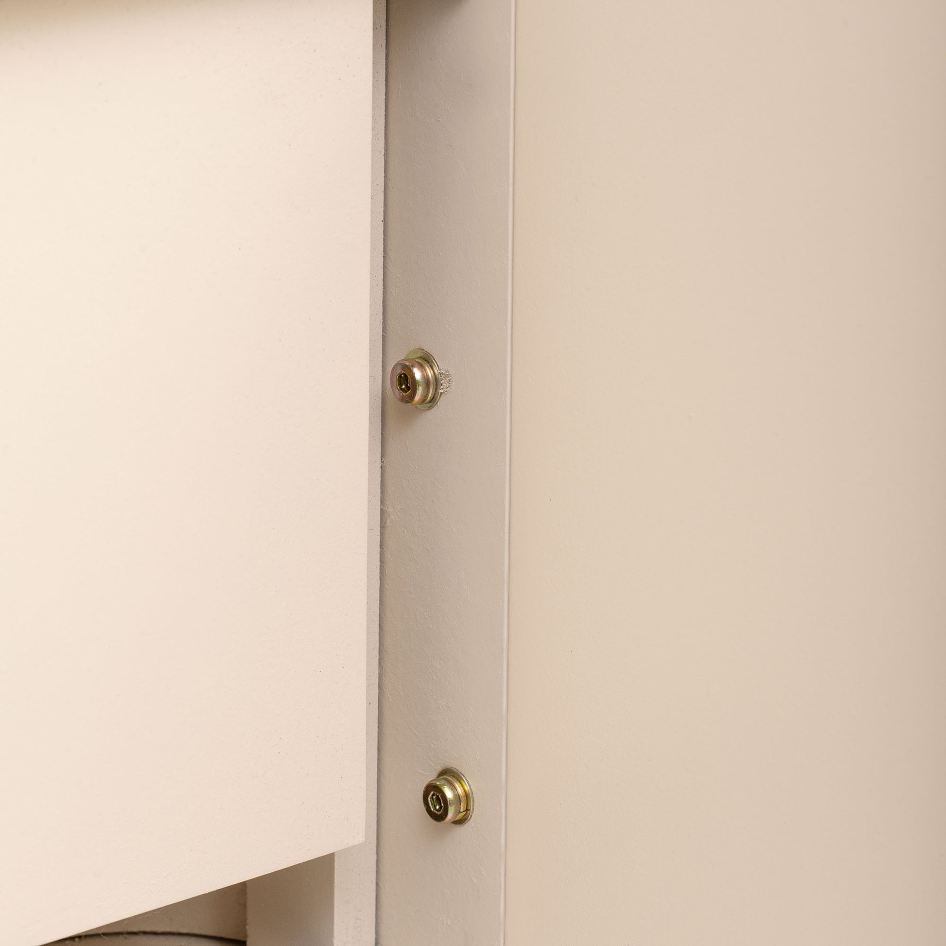 Closeup of beige cabinet panel showing two silver cam lock fasteners for assembly