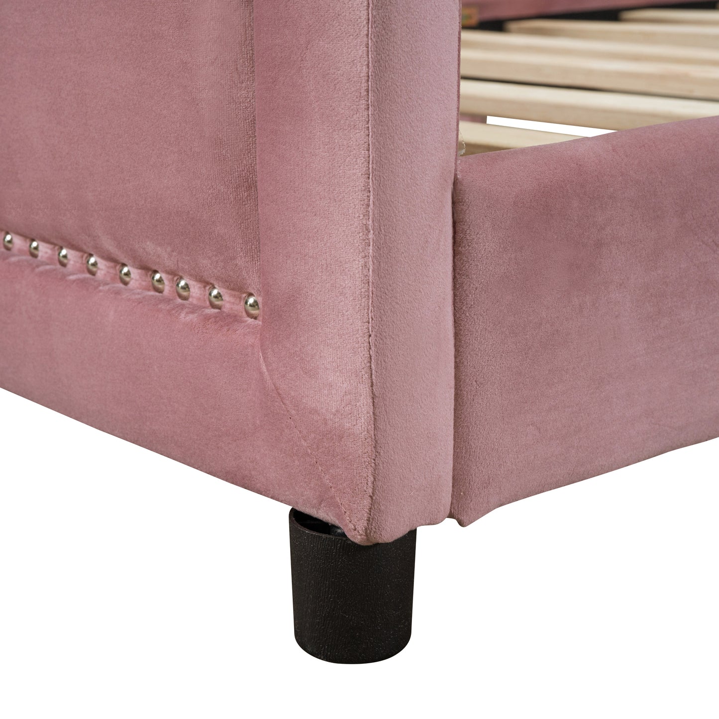 Pink velvet bed frame detail with silver nailhead trim and dark wooden leg