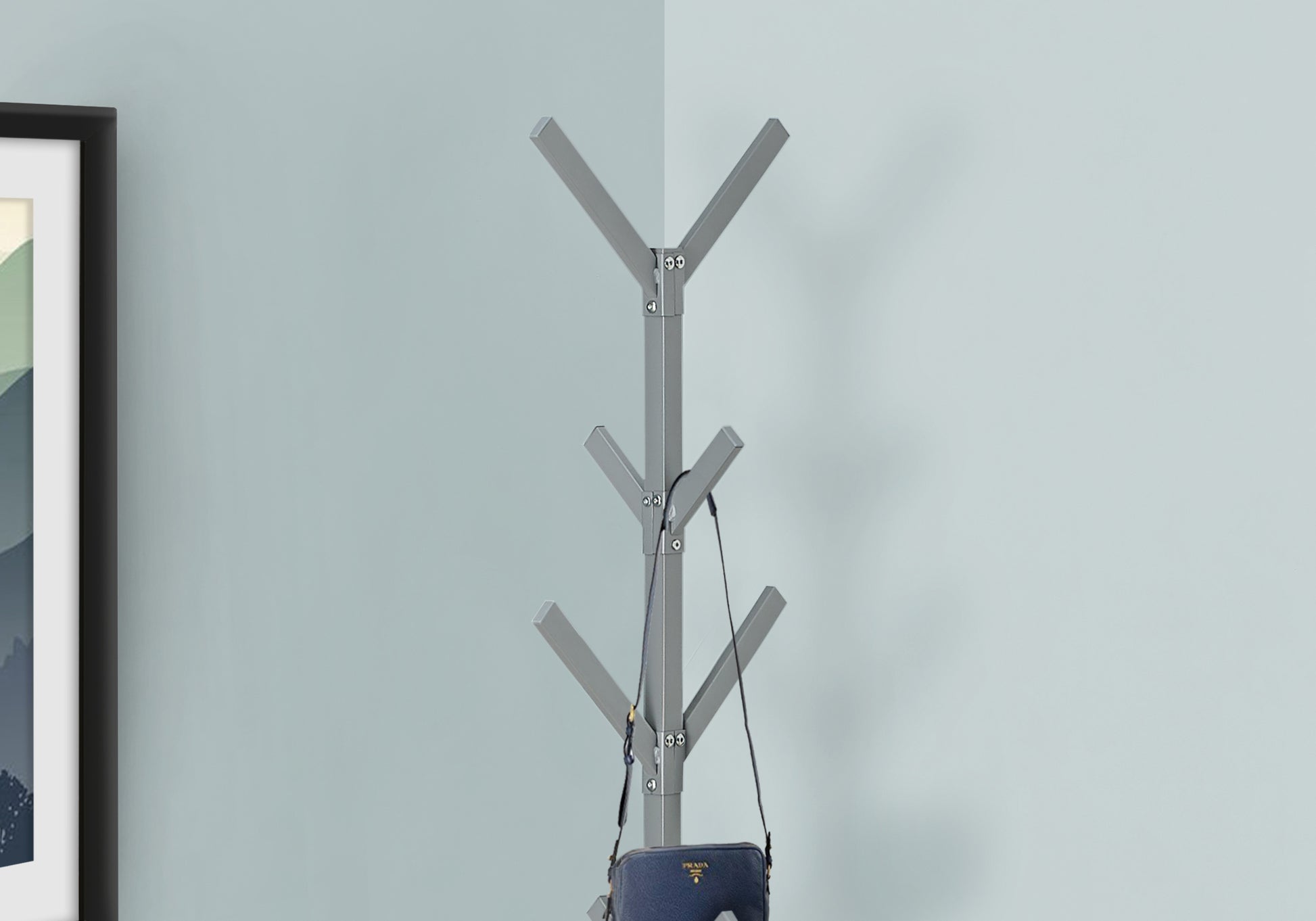 Modern grey metal coat rack with multiple branches holding a navy handbag