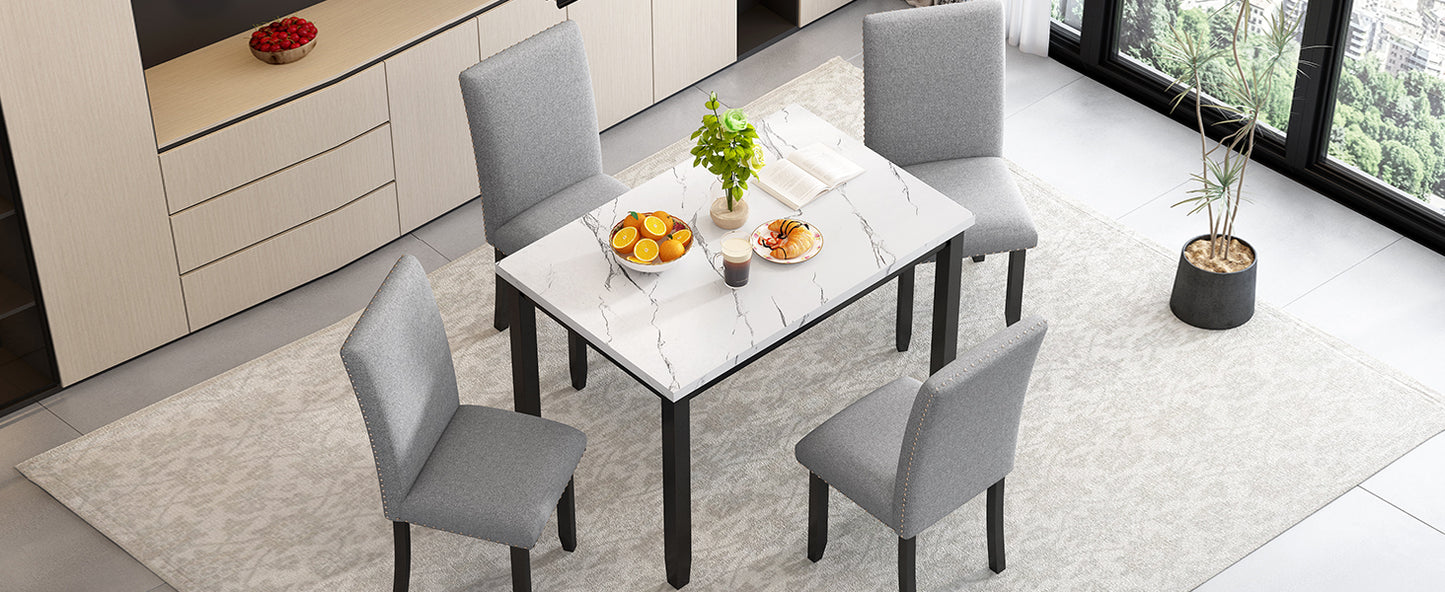 Grey upholstered dining chairs with nailhead trim surround a white marbletop dining table