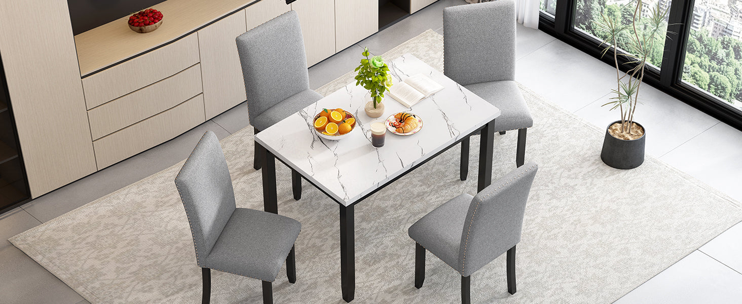 Grey upholstered dining chairs with nailhead trim surround a white marbletop dining table