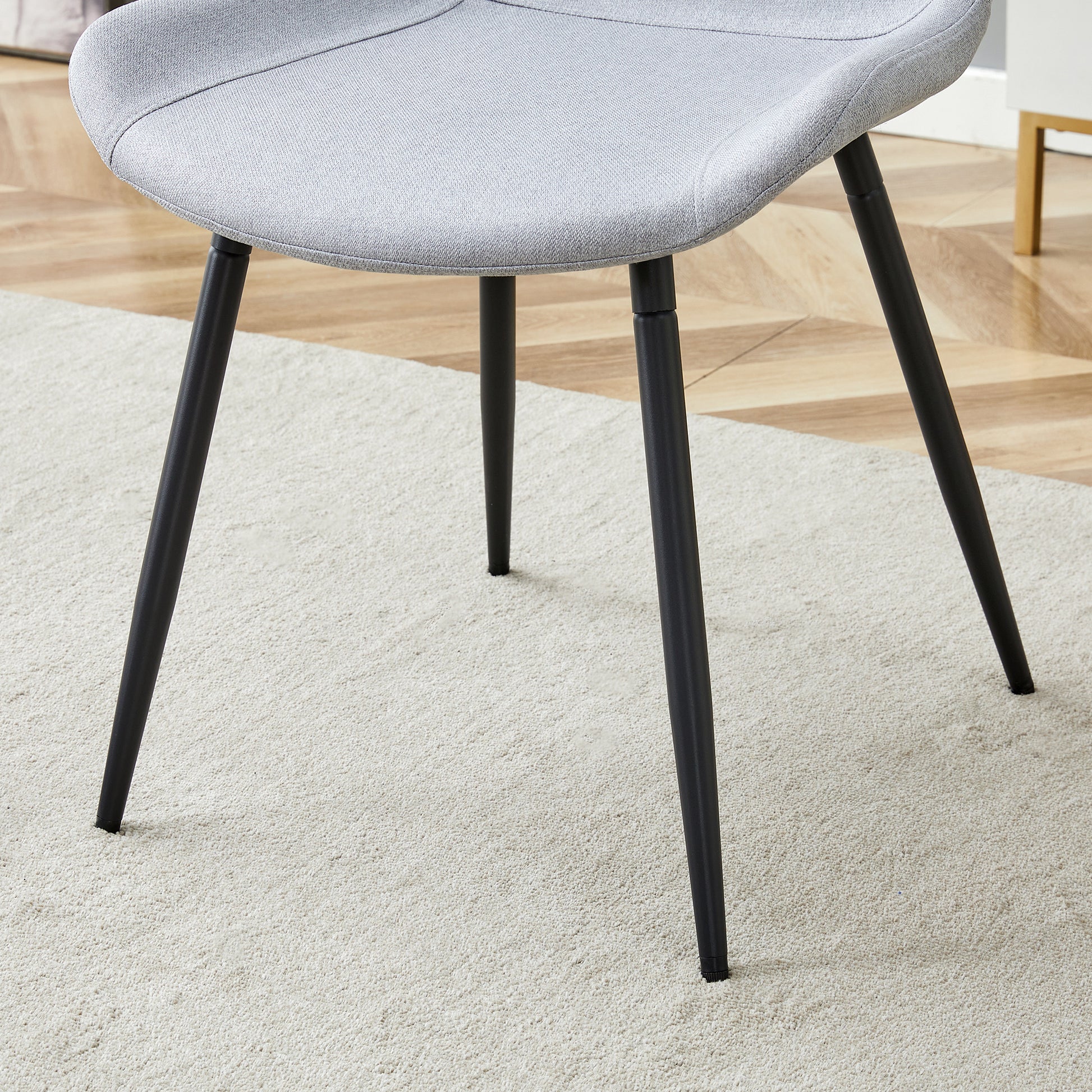 Light gray fabric dining chair with black metal legs on a cream rug
