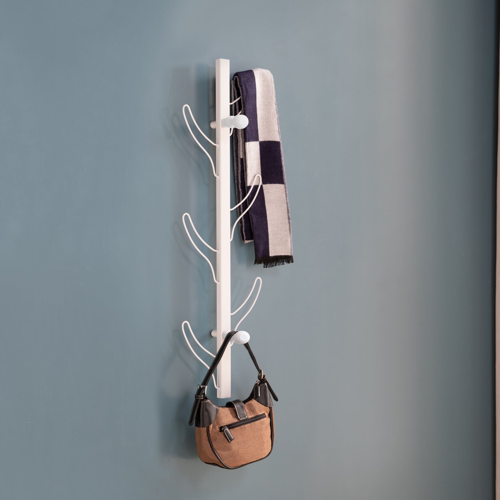 White wallmounted coat rack with brown handbag and blue checkered scarf