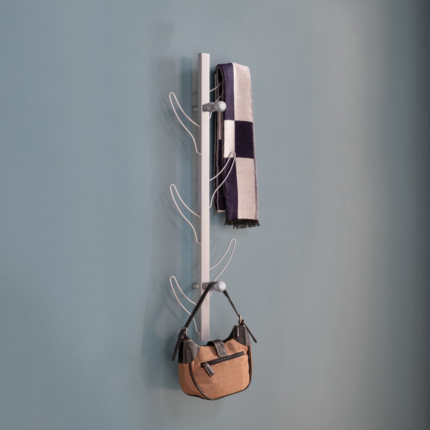 Modern silver wallmounted coat rack with checkered scarf and tan handbag