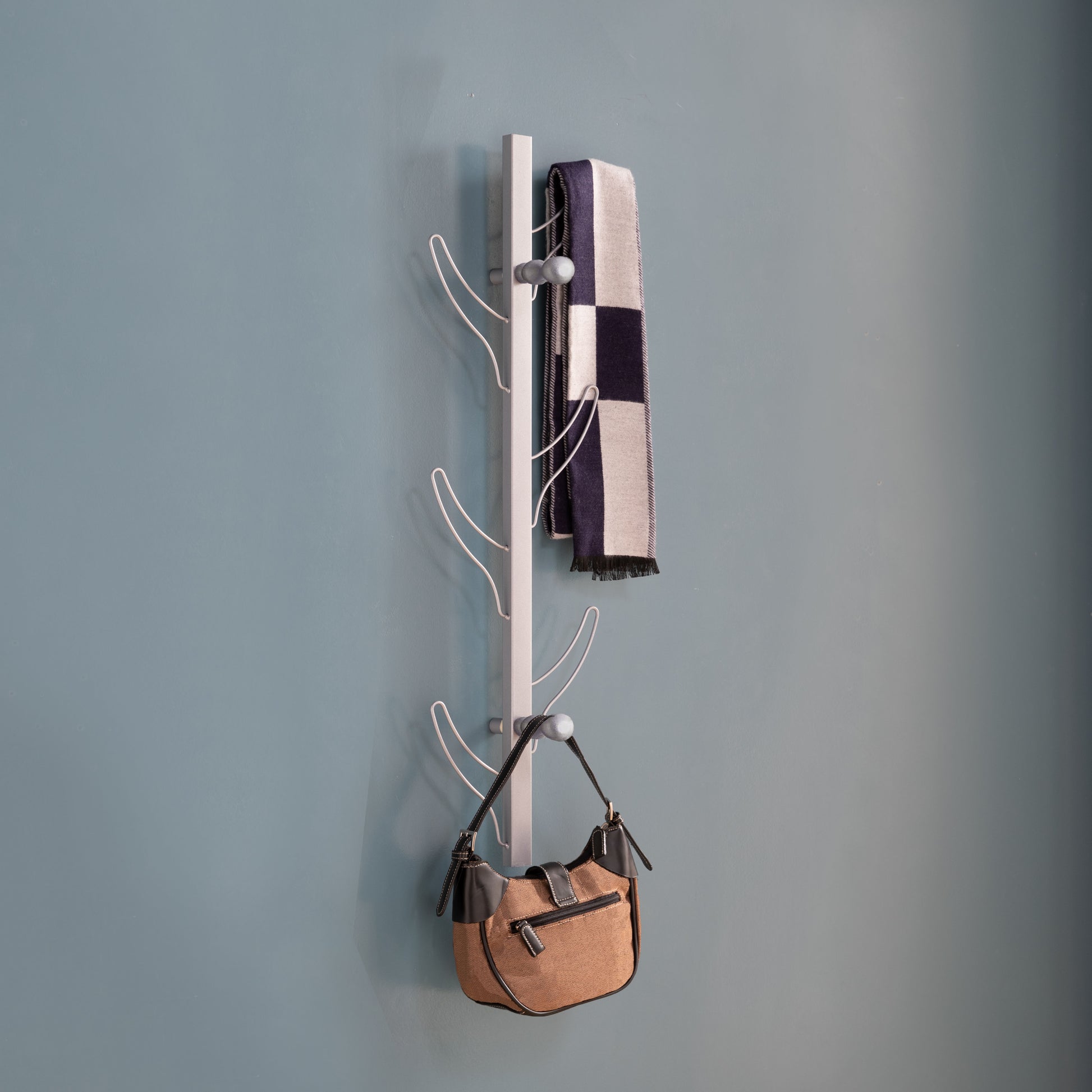 Modern silver wallmounted coat rack with checkered scarf and tan handbag