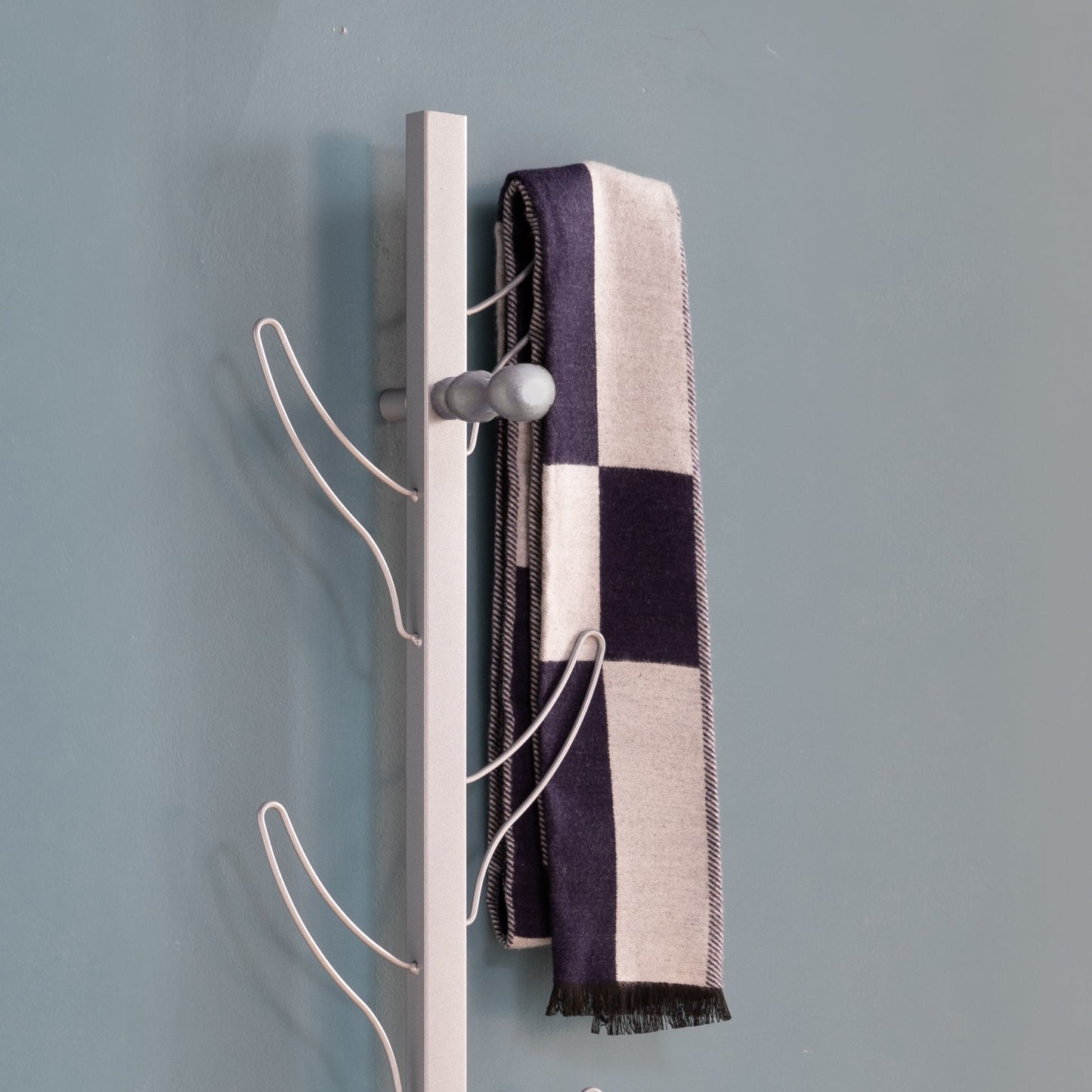 Gray metal coat rack holding a checkered navy and cream scarf