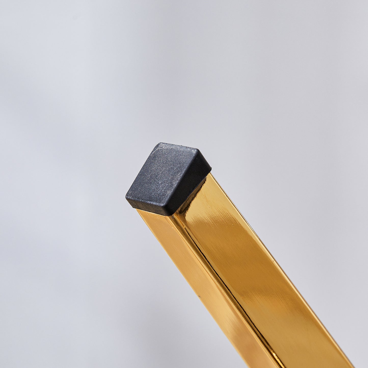 Square black protective cap on a polished gold metal furniture leg